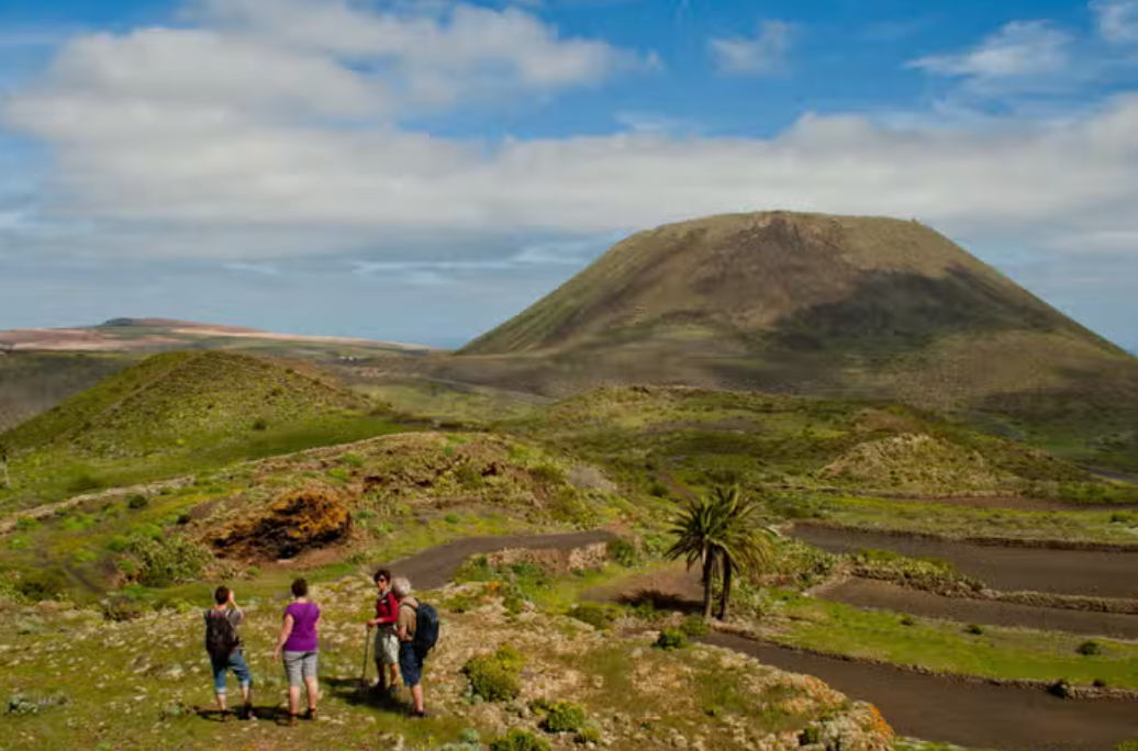 Un viaggio di gruppo WeRoad per quattro persone in escursione su un sentiero attraverso un paesaggio verde e collinare, con un grande cono vulcanico in lontananza.