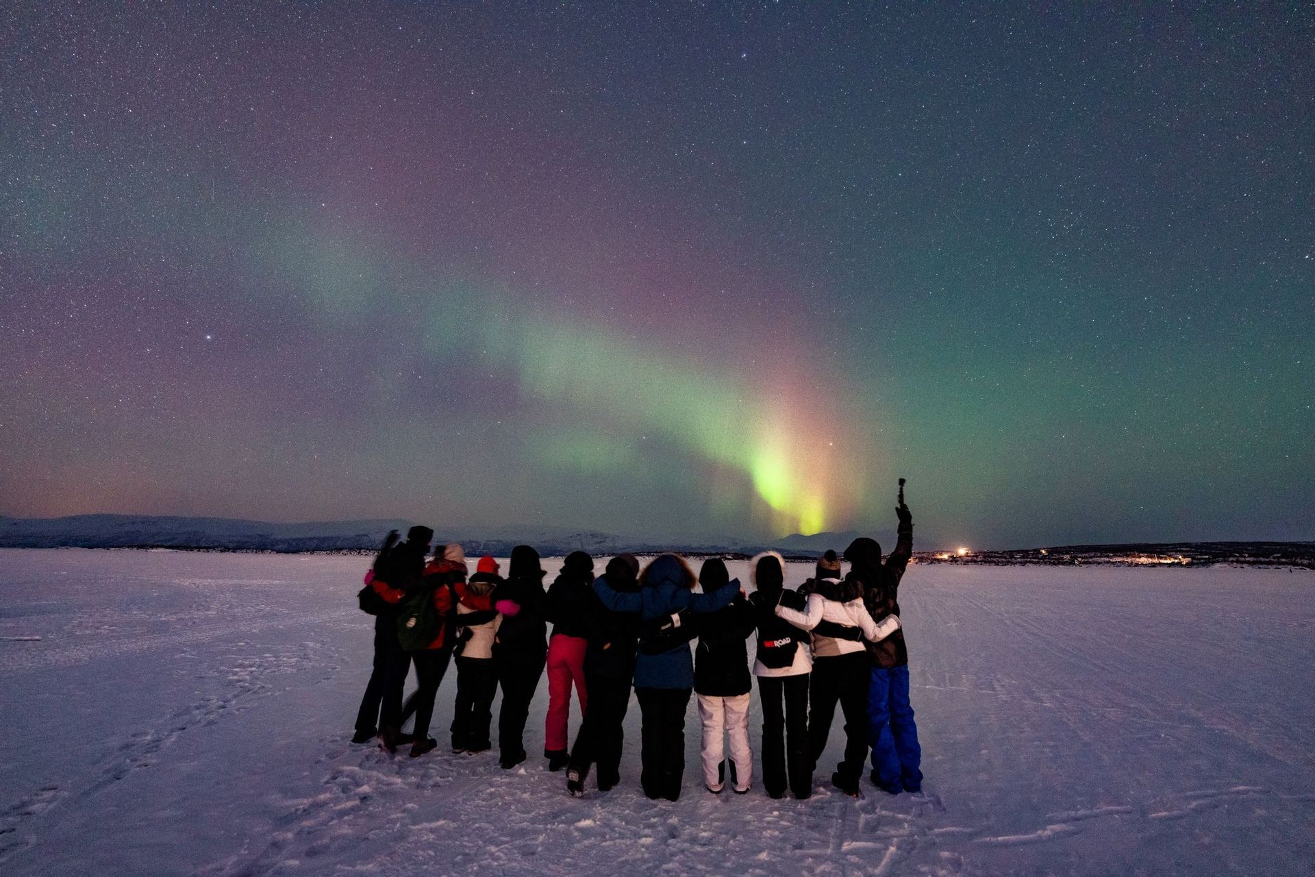Un groupe WeRoad réuni dans un paysage enneigé la nuit, observant les aurores boréales sous un ciel étoilé.