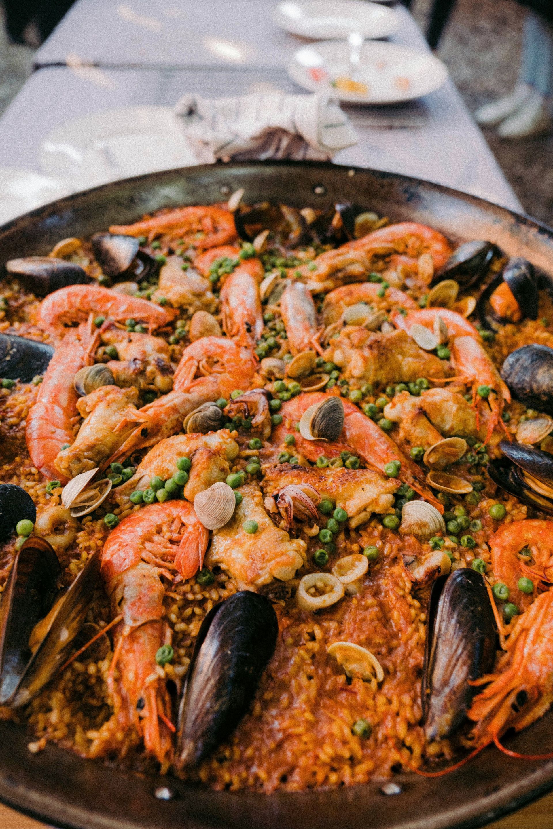 Primo piano di una paella tradizionale in una grande padella, ricca di riso, gamberi, cozze, pollo e piselli.
