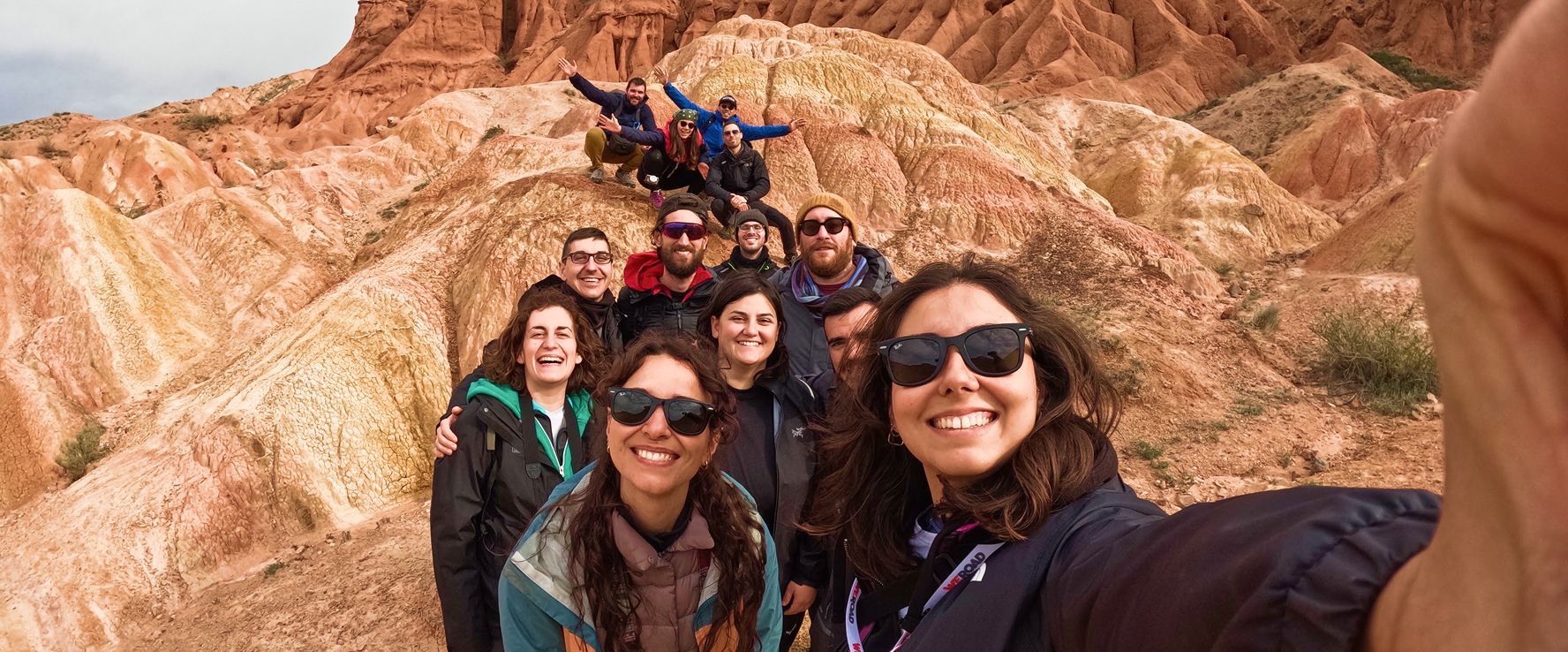 Eine WeRoad-Gruppe lächelt für ein Selfie, posierend auf den farbenfrohen Hügeln eines roten Felsencanyons.