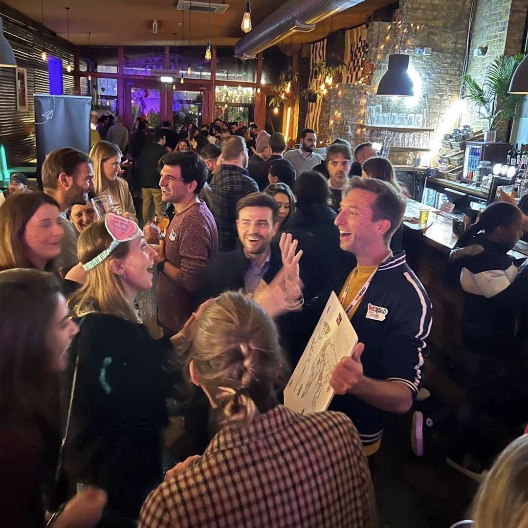 Un gran grupo de personas de WeRoad riendo y socializando juntos dentro de un bar concurrido y cálidamente iluminado durante un evento.