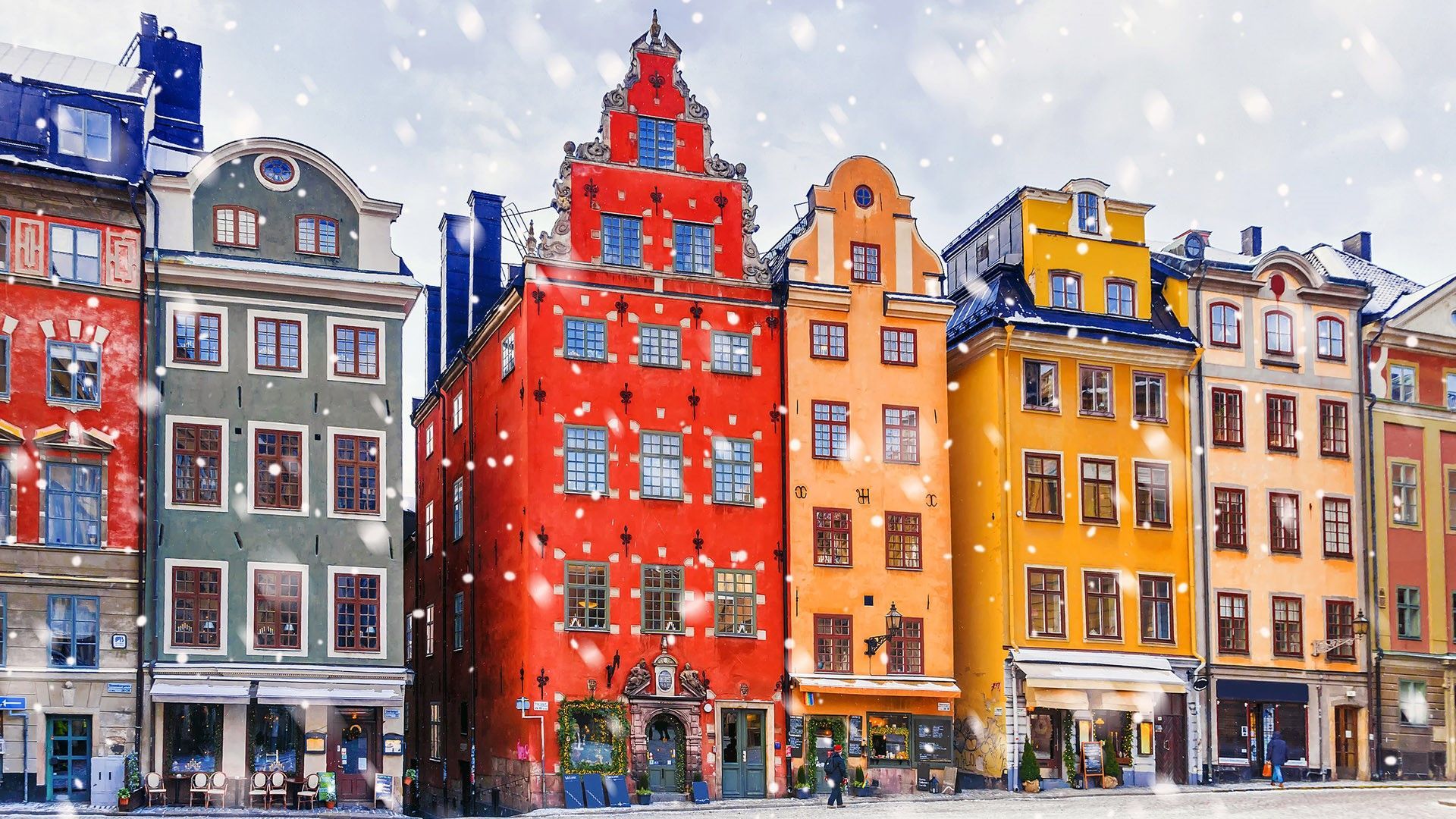 Una fila di edifici colorati e storici in stile europeo che costeggiano una strada acciottolata mentre cade la neve.