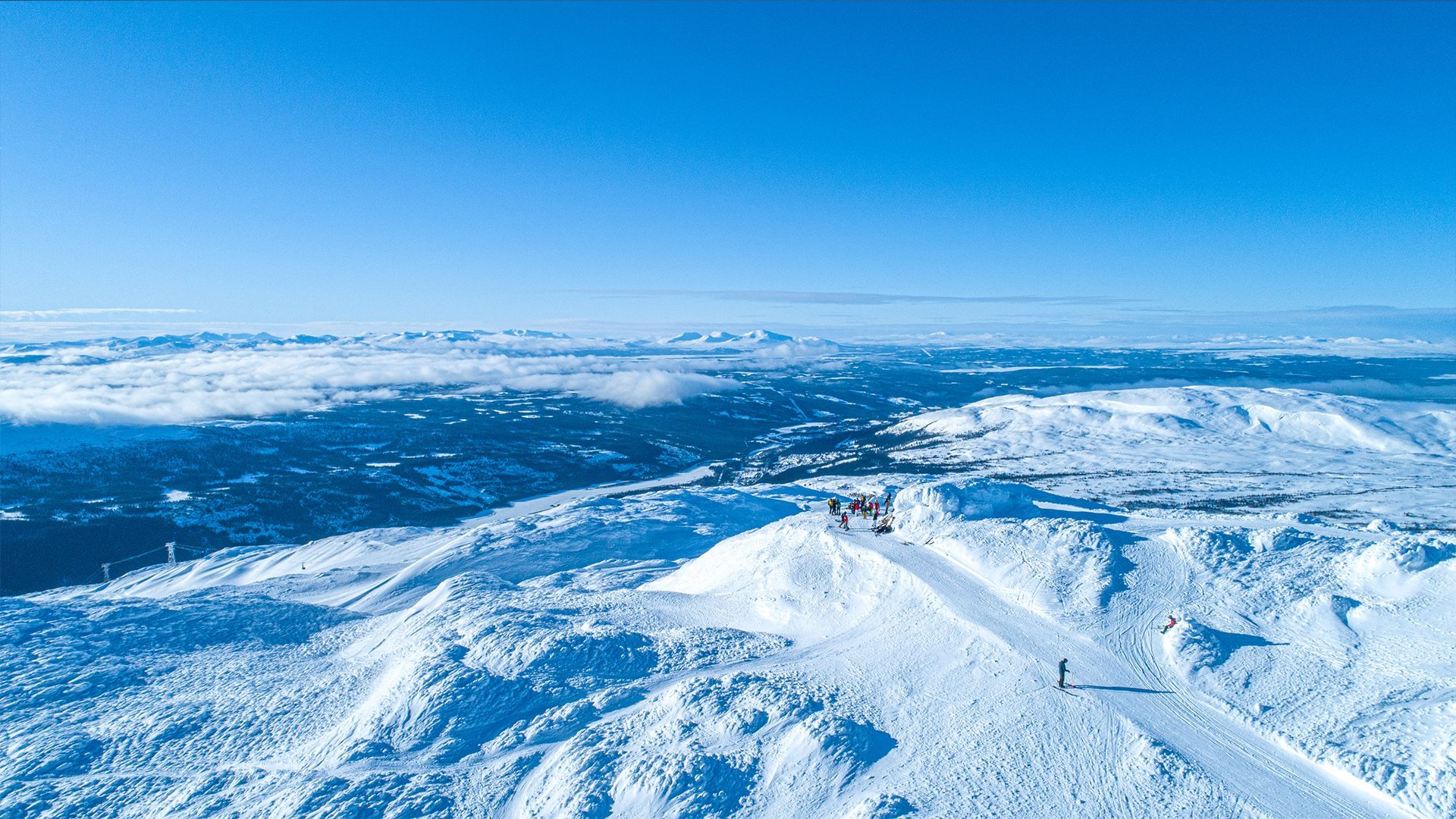 Una vista aerea di un viaggio di gruppo WeRoad su una cima di montagna innevata, che si affaccia su un vasto paesaggio invernale illuminato dal sole sotto un cielo azzurro e limpido.