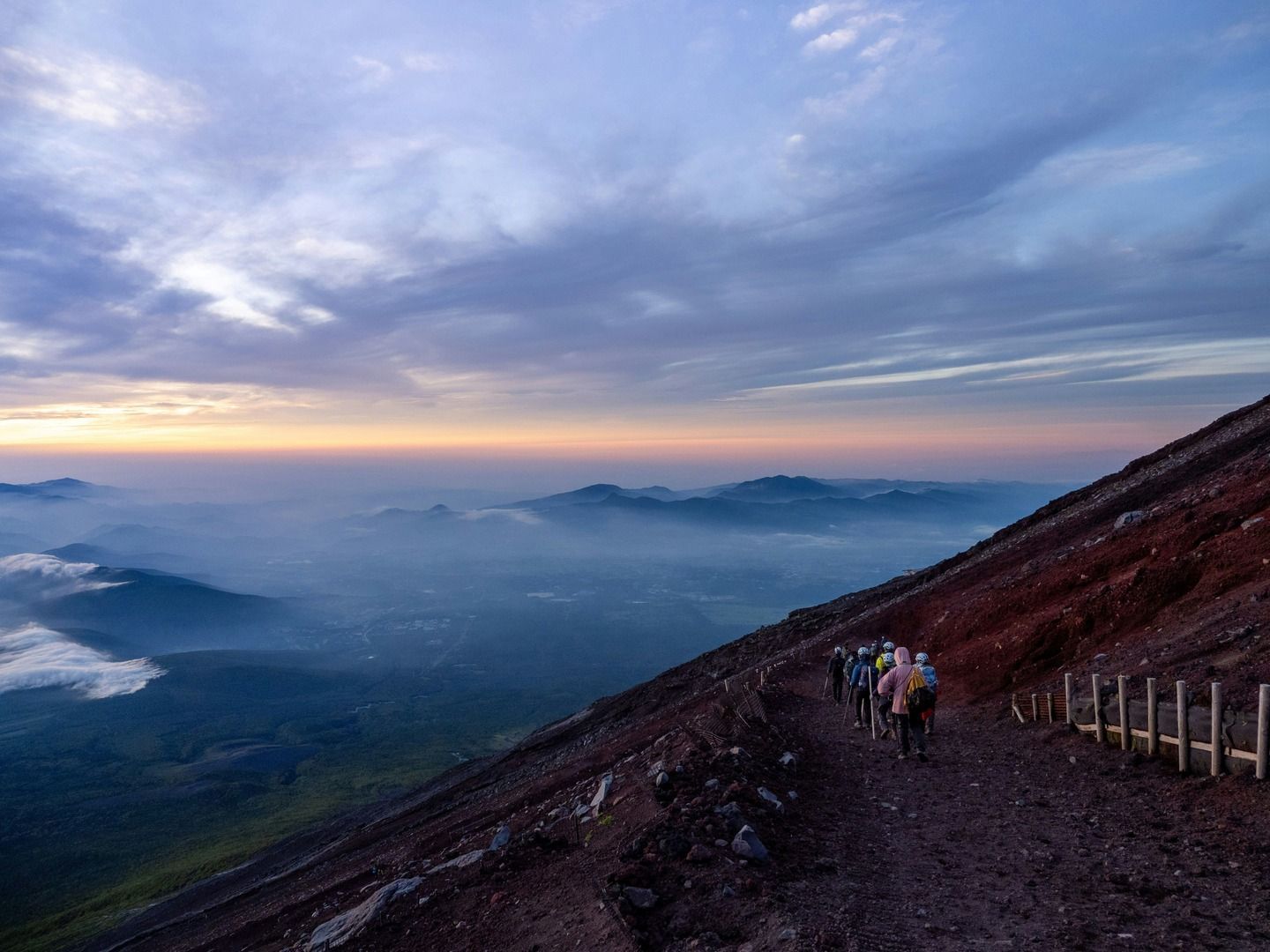 Un gruppo WeRoad in escursione su un ripido sentiero di montagna all'alba, con vista su una vasta e nebbiosa catena montuosa.