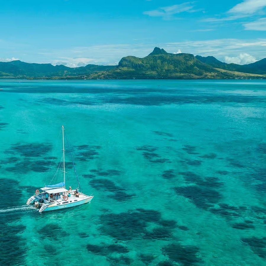 Veduta aerea di un catamarano con a bordo un gruppo WeRoad che naviga su acque turchesi verso un'isola montuosa.