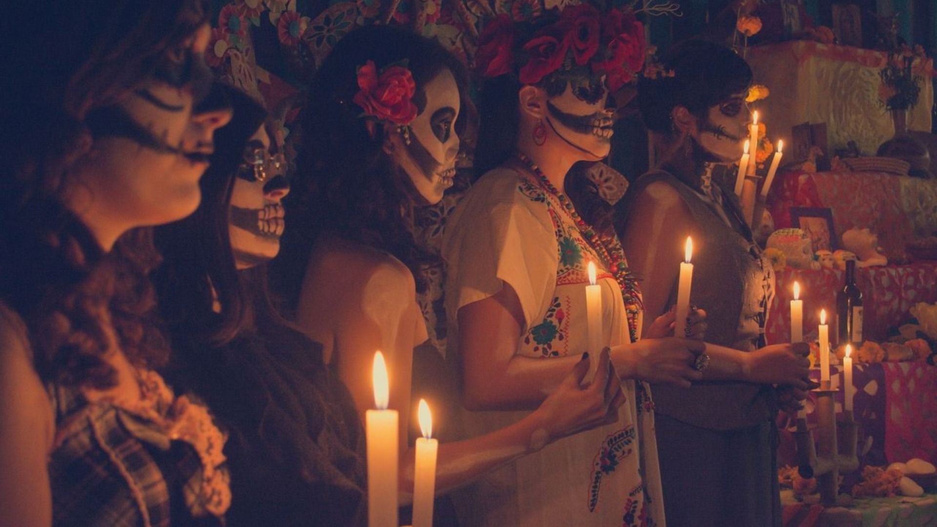 A WeRoad group trip of women with skull face paint and flower crowns holding lit candles in a dimly lit room.