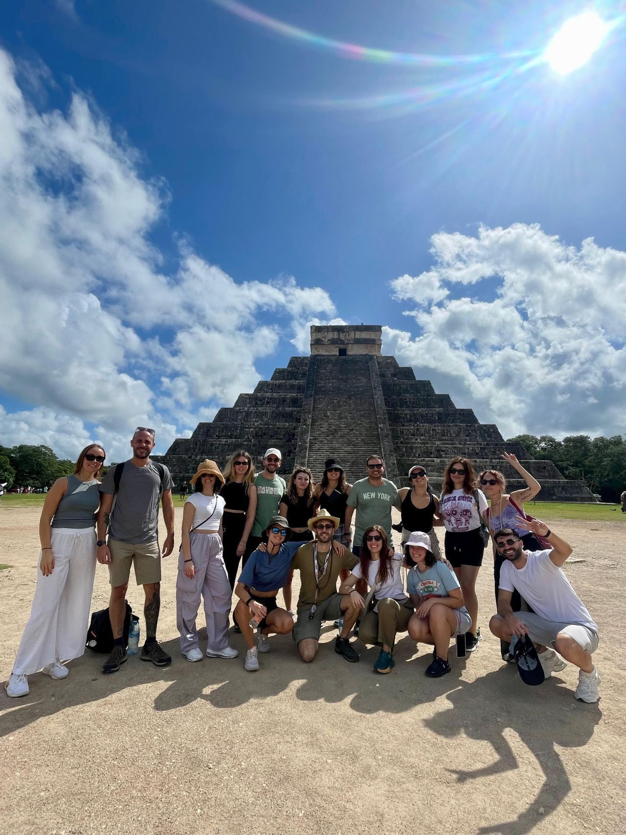 Un viaggio di gruppo WeRoad in posa per una foto davanti a una grande piramide di pietra sotto un cielo soleggiato con nuvole sparse.