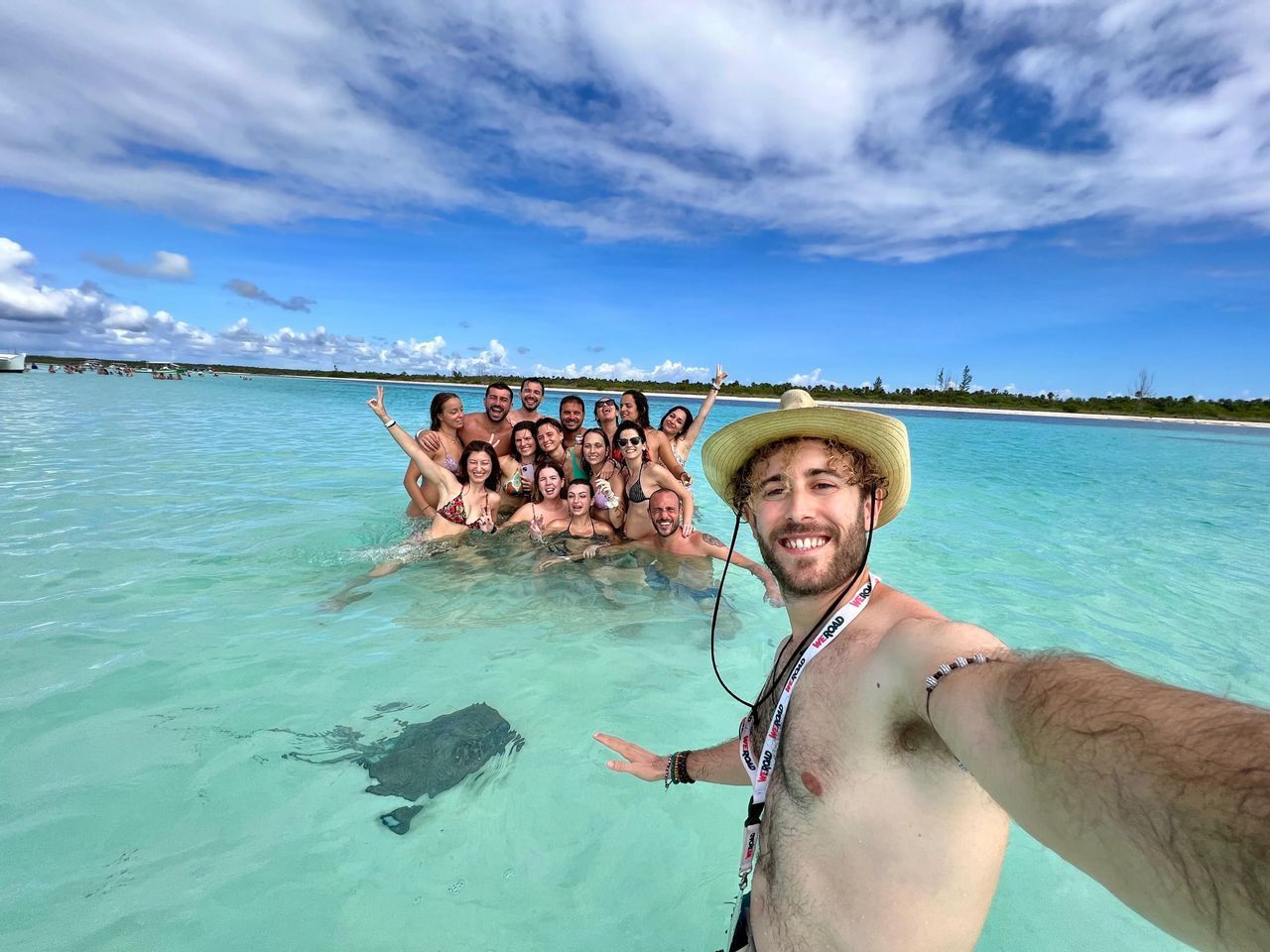 Un uomo si scatta un selfie con un viaggio di gruppo WeRoad e una razza che nuota in acqua cristallina turchese sotto un cielo azzurro.