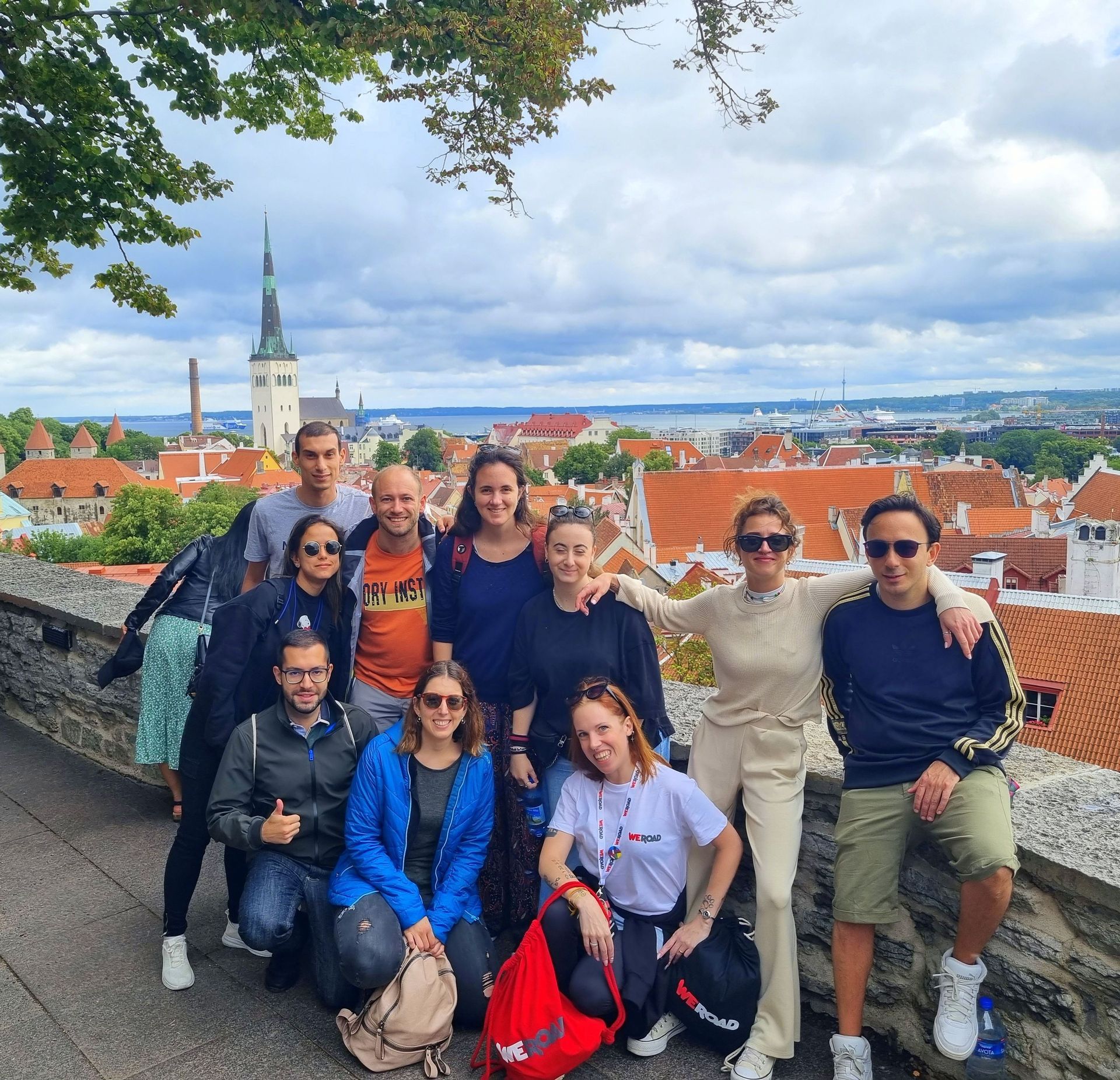 Un gruppo WeRoad in posa per una foto da un punto panoramico in pietra che domina una città con tetti rossi e un campanile.