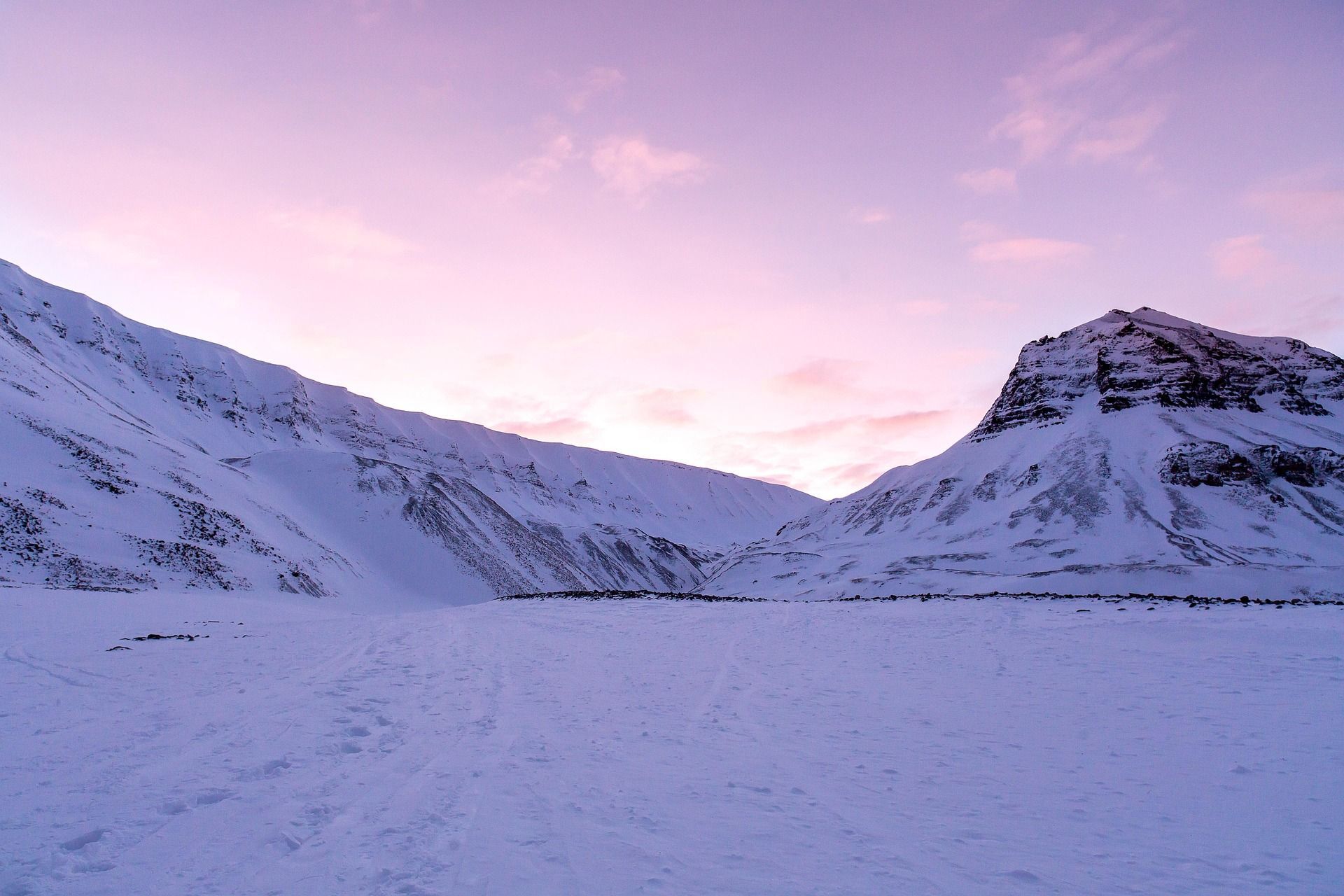 Un vasto valle cubierto de nieve anidado entre montañas bajo un cielo rosa y morado al atardecer.