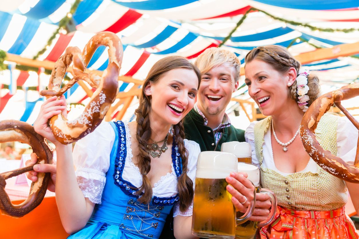 A WeRoad group trip of people in traditional outfits laughing together while holding large beers and pretzels.