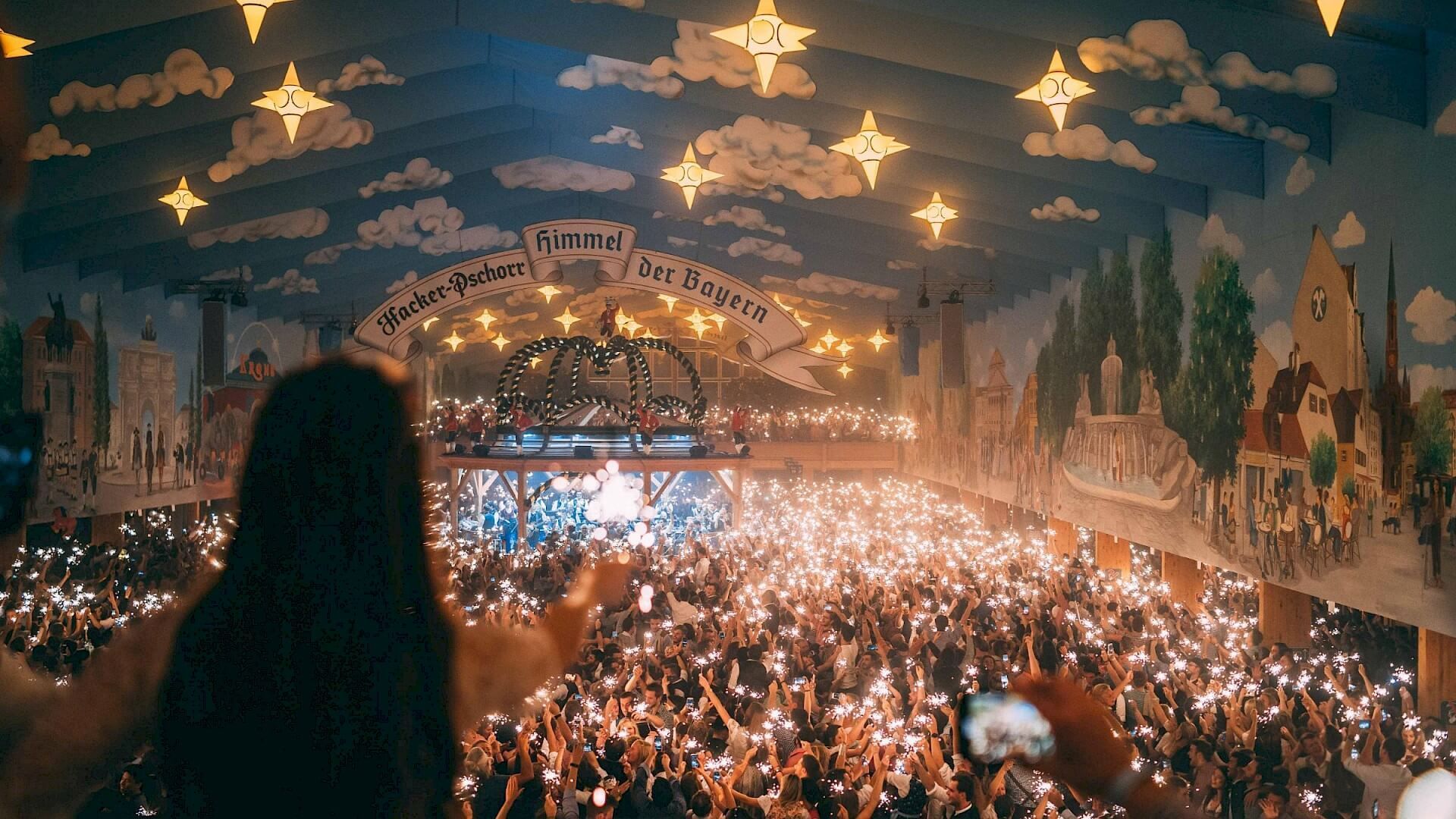 A large crowd fills a festive hall, holding up thousands of lit sparklers that illuminate the room.