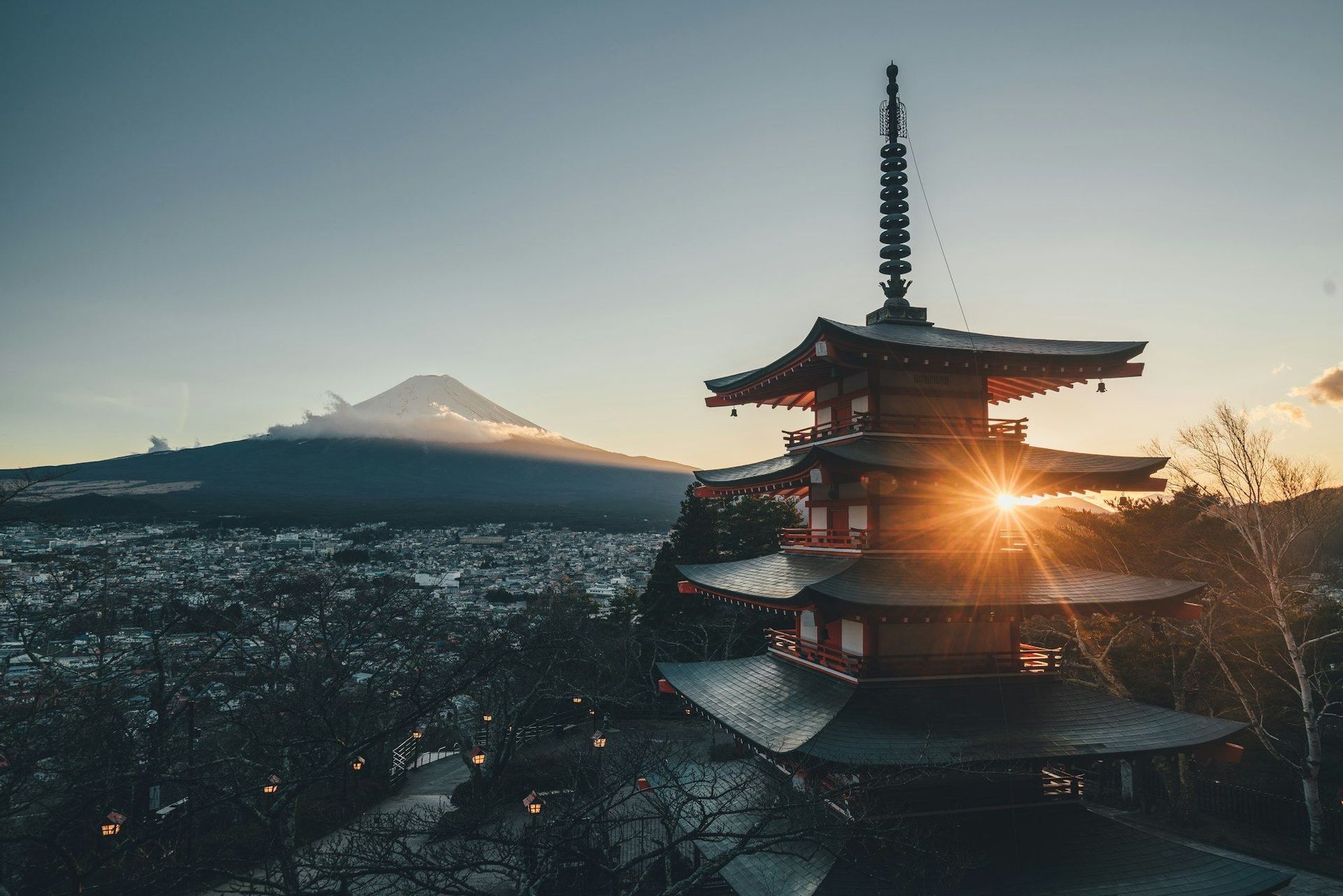 Au lever du soleil, une pagode rouge surplombe une ville, avec le mont Fuji enneigé en arrière-plan, créant un effet d'explosion solaire.