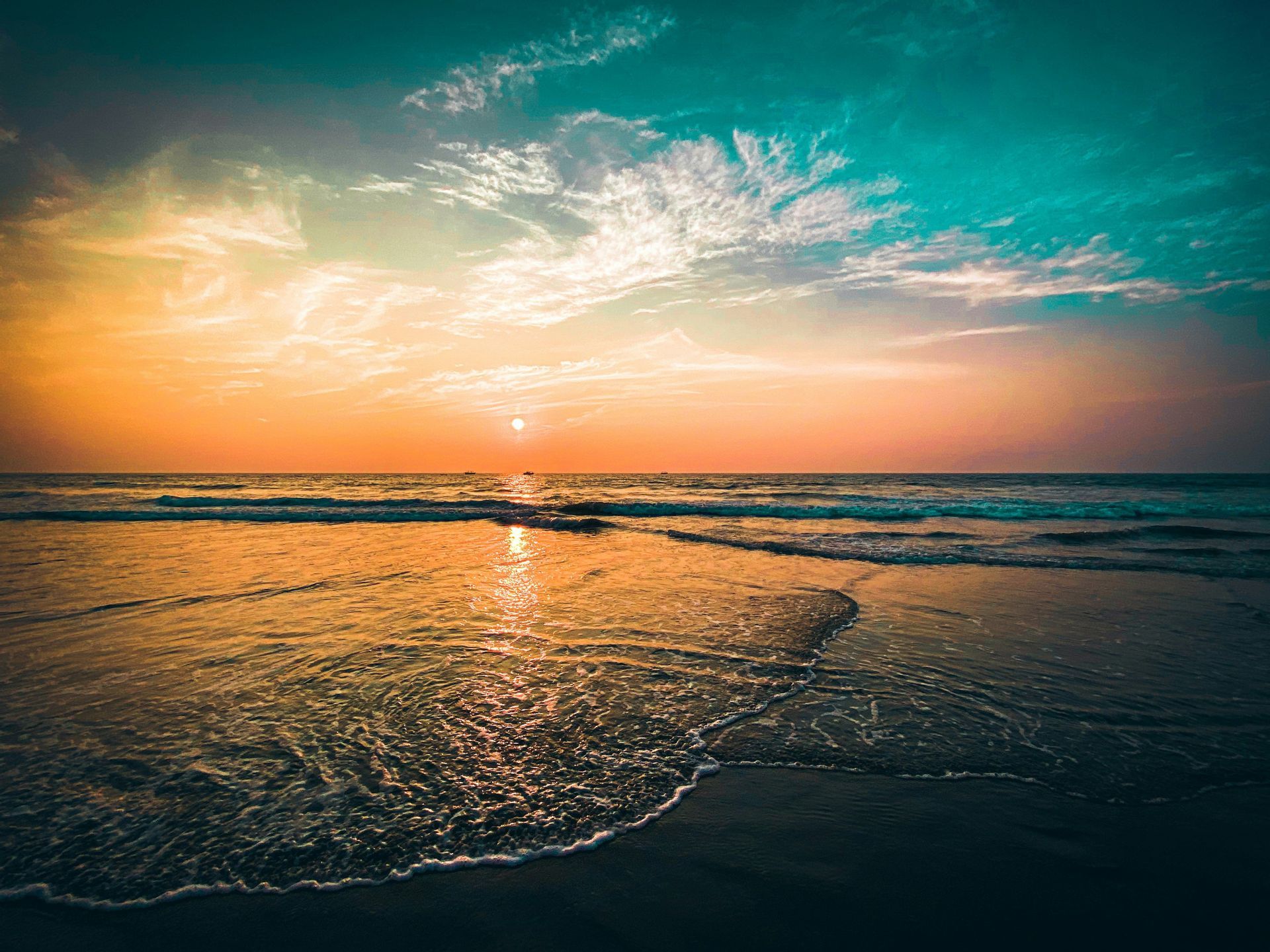 Il sole tramonta sull'oceano, la sua luce si riflette sull'acqua mentre dolci onde bagnano la sabbia umida su una spiaggia.