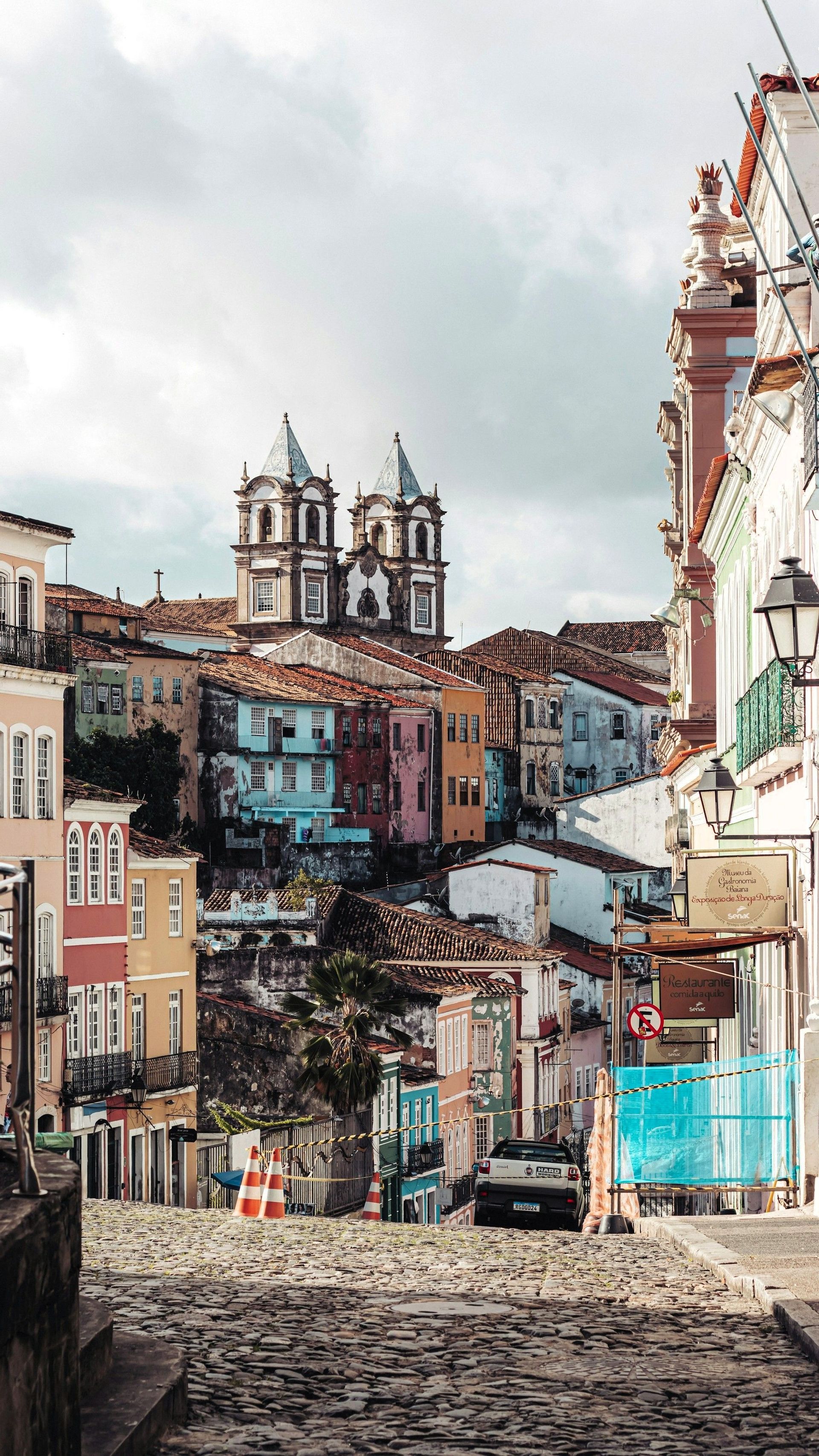 Eine Kopfsteinpflasterstraße führt abwärts durch eine Stadt mit farbenfrohen, historischen Gebäuden und einer im Hintergrund sichtbaren Kirche.