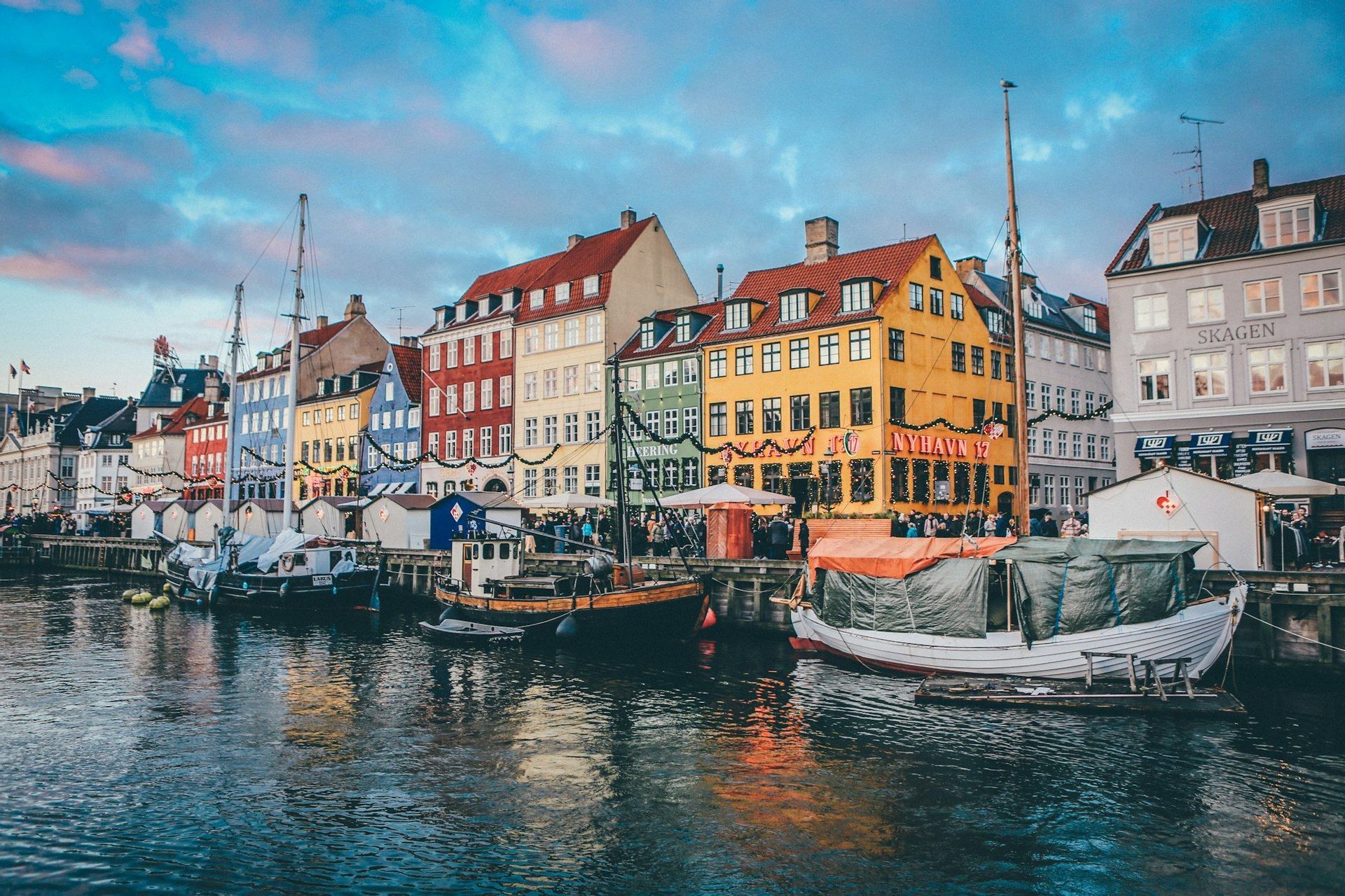 Des bateaux sont amarrés le long d'un canal devant une rangée de bâtiments colorés au coucher du soleil.