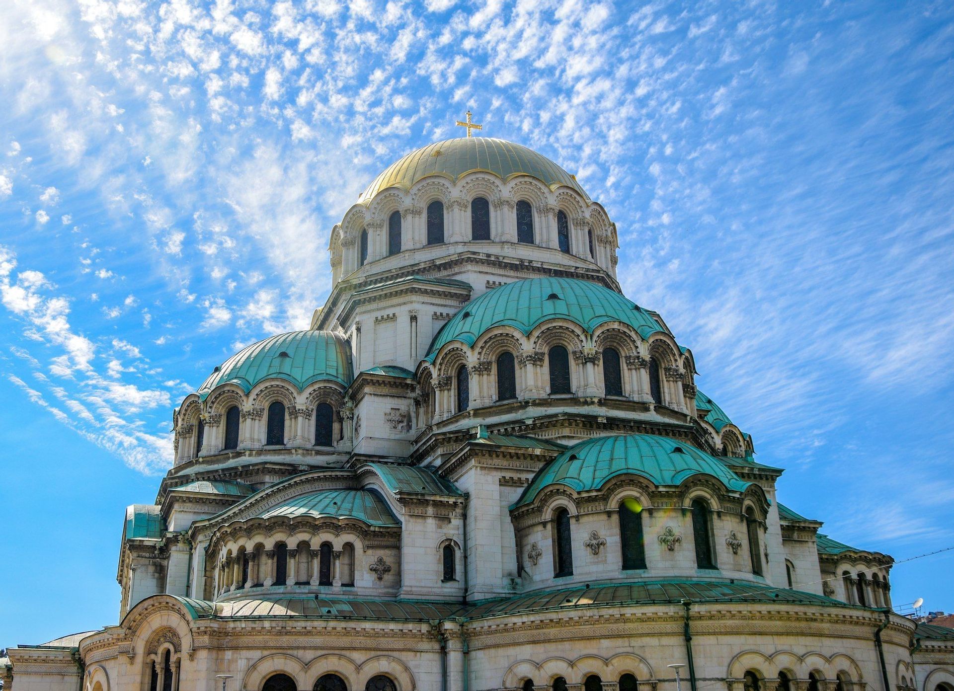 Una grande cattedrale con una cupola centrale dorata e cupole verdi più piccole si erge sotto un cielo azzurro brillante con nuvole sottili.