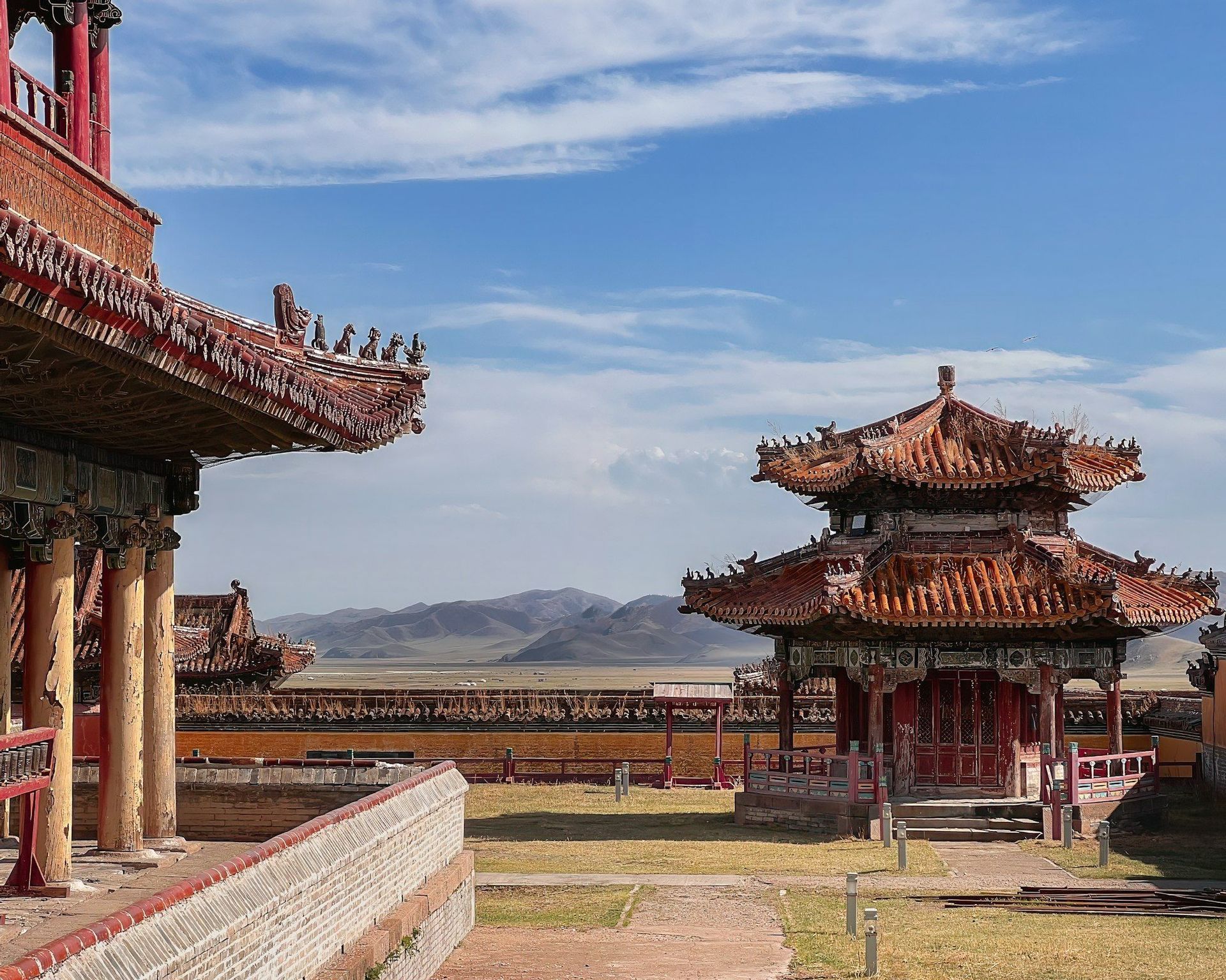 Una pagoda tradizionale e edifici con tetti rossi in un cortile con un paesaggio montano sullo sfondo sotto un cielo azzurro.