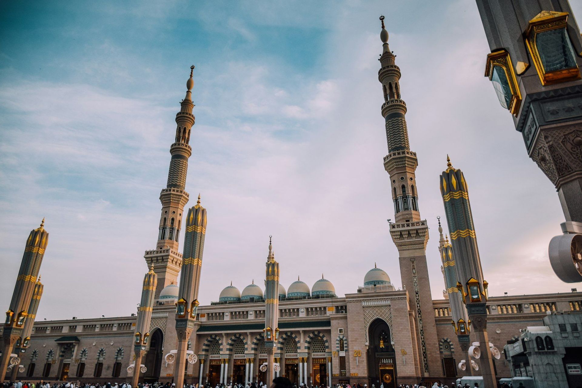 Una vista dal basso di una grande moschea con minareti imponenti e diverse cupole, mentre una folla si raduna nel cortile.