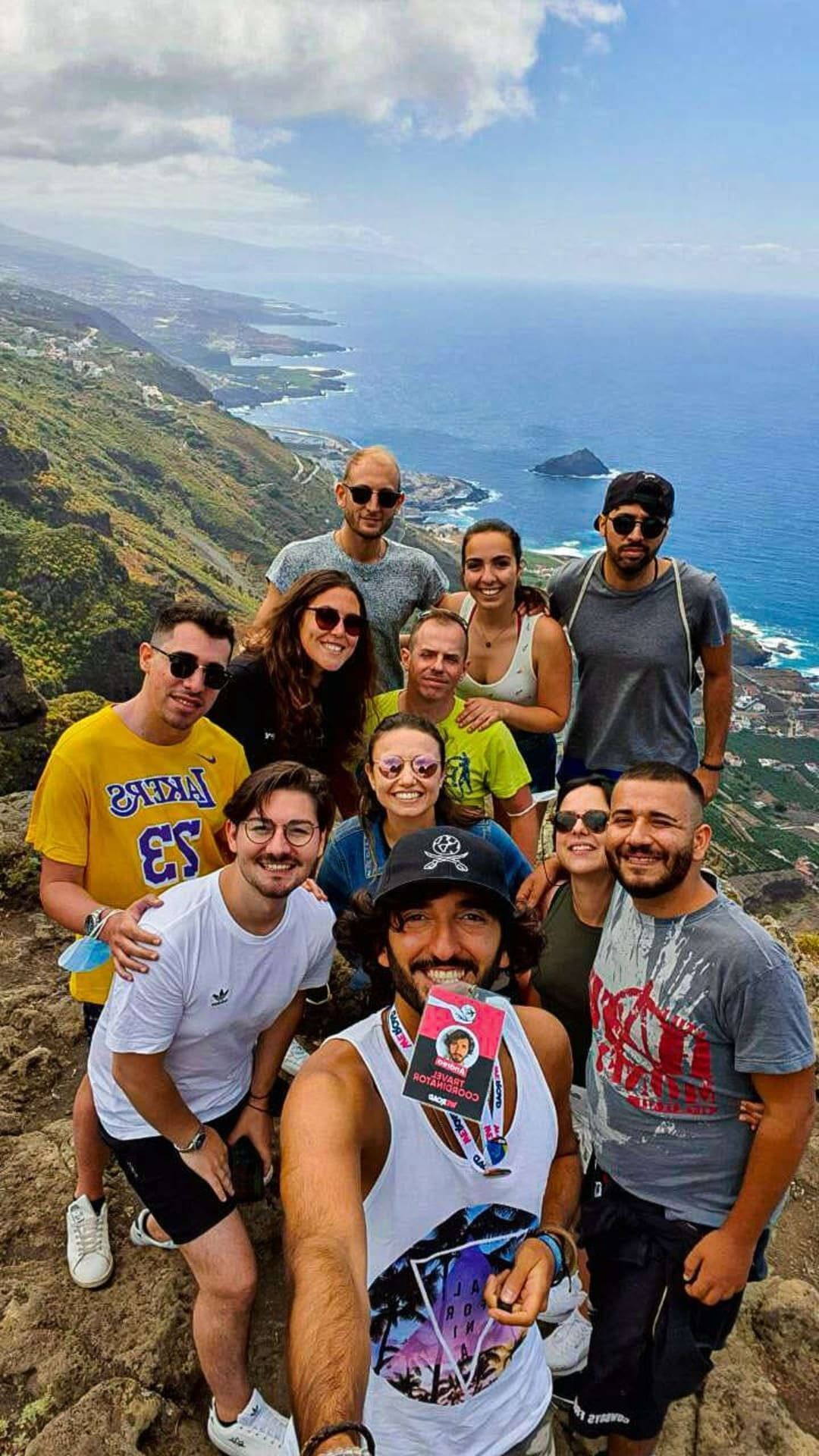Eine WeRoad-Reisegruppe macht ein Gruppenselfie auf einer Klippe mit Panoramablick auf die darunterliegende Küste und das Meer.