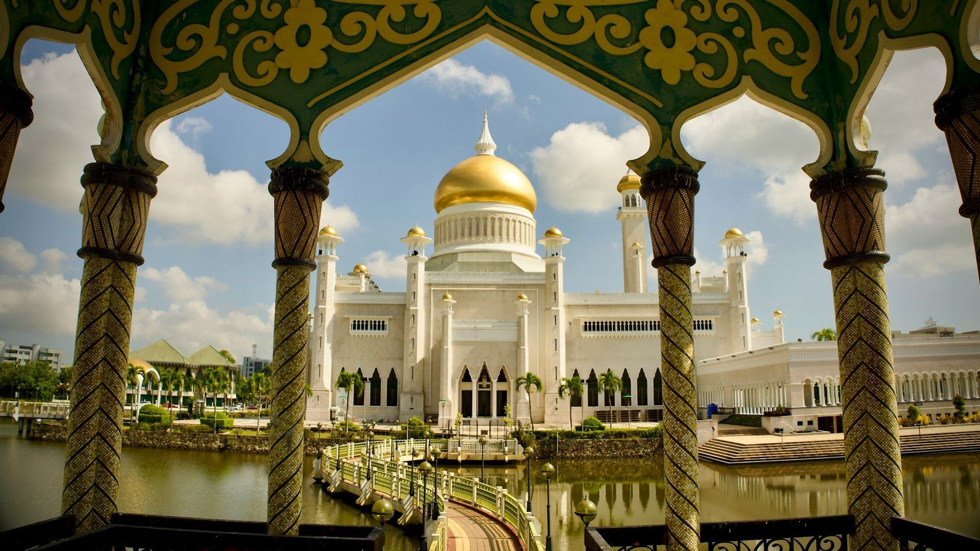 Una vista di una moschea bianca con una grande cupola dorata, incorniciata da colonne decorative e un arco verde e oro.