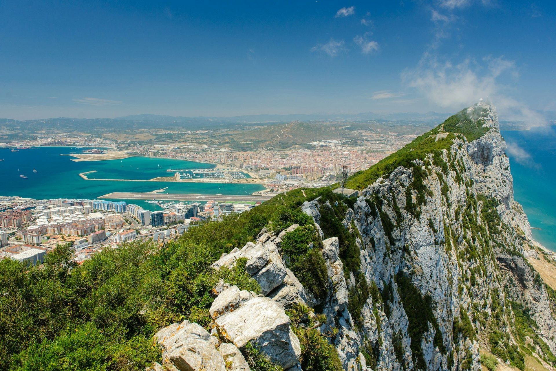 Vista mozzafiato da una scogliera ripida e rocciosa, ricoperta di vegetazione, che domina una città costiera, un porto e il mare.