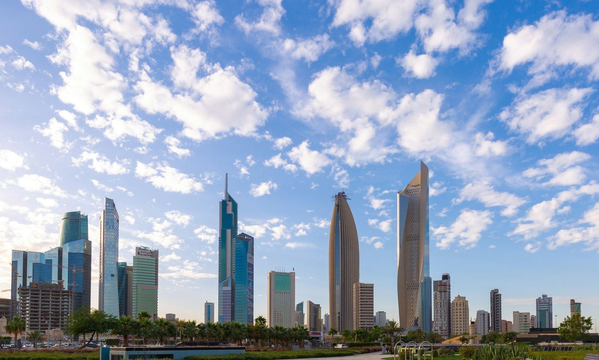 Una vista panoramica dello skyline di una città moderna con grattacieli di vetro unici sotto un cielo blu con nuvole bianche sparse.