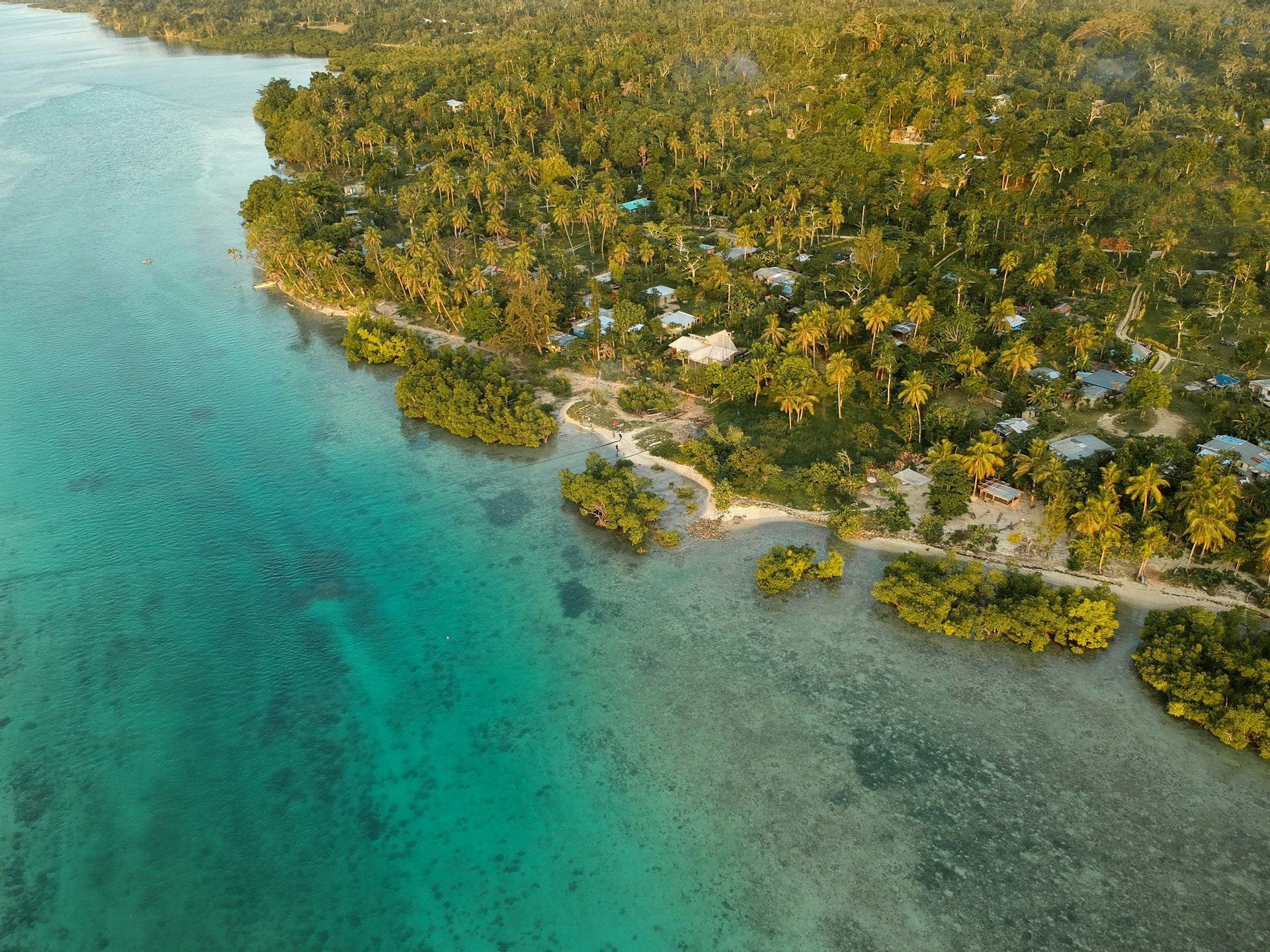 Vista aerea di un piccolo villaggio costiero immerso in una lussureggiante foresta tropicale accanto a acque limpide e turchesi.