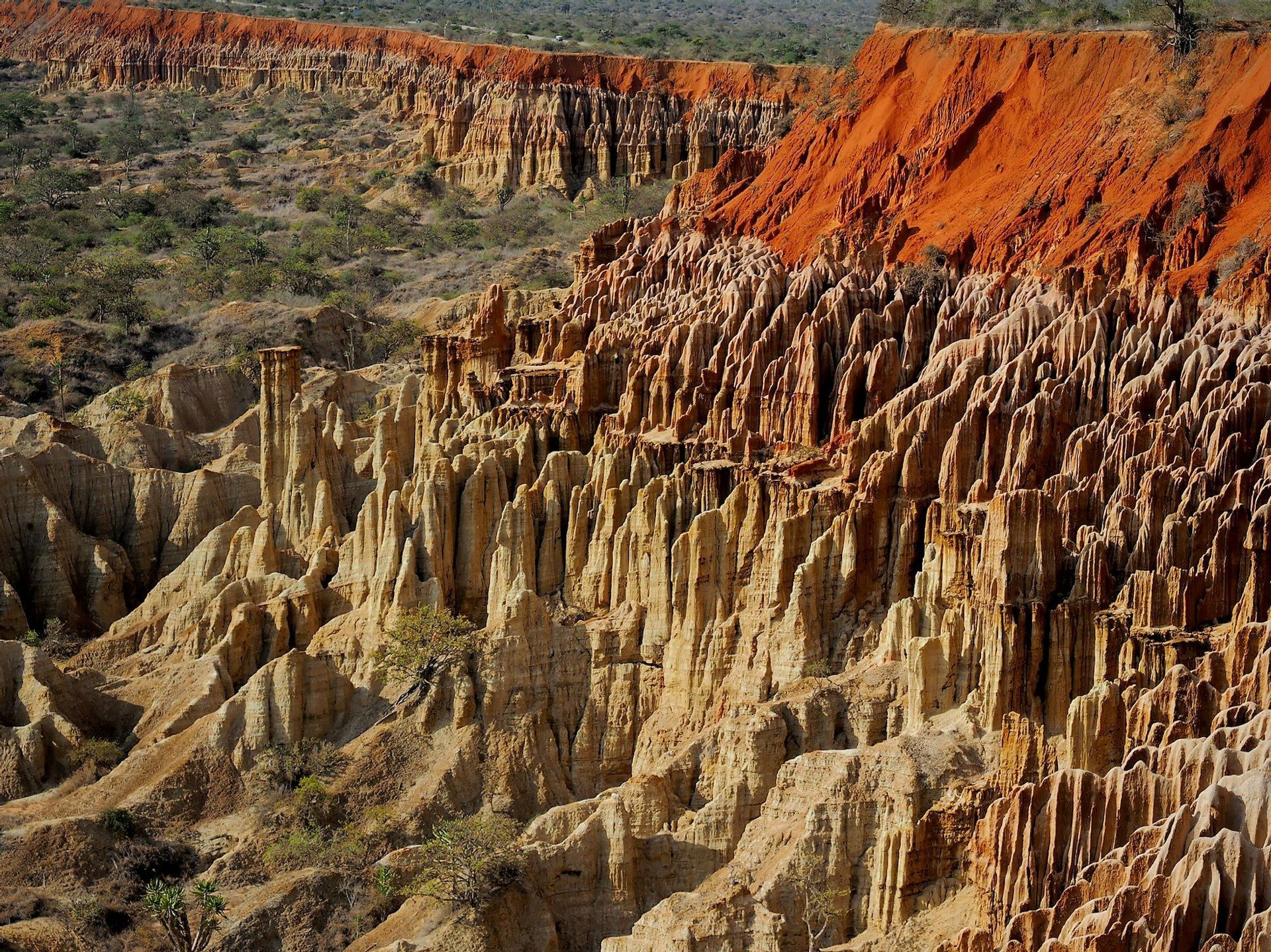Un paisaje de formaciones de arenisca erosionada que crean un cañón, con una capa superior distintiva de tierra roja sobre pináculos de tonos más claros.