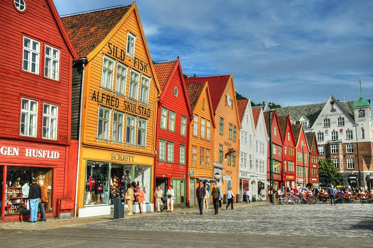 A row of colorful traditional wooden buildings with gabled roofs on a cobblestone street, with people walking in front.