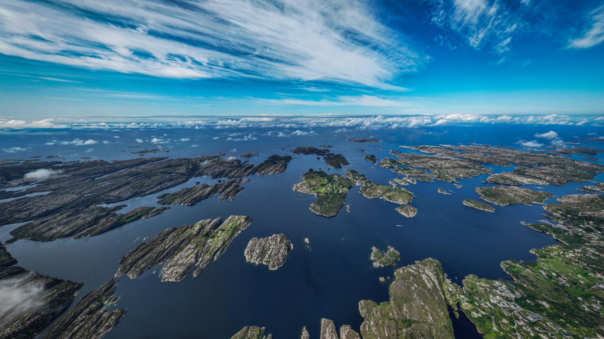 An aerial view of a vast archipelago of rocky, green islands surrounded by deep blue water under a partly cloudy sky.