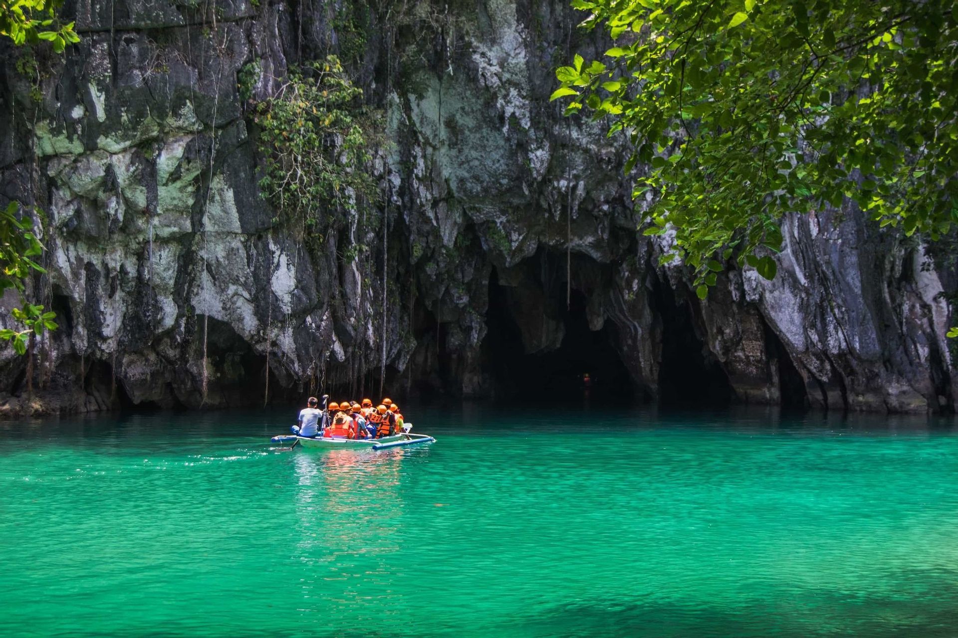 Un viaggio di gruppo WeRoad in barca a remi su acque turchesi verso l'ingresso di una grande grotta in una scogliera rocciosa.