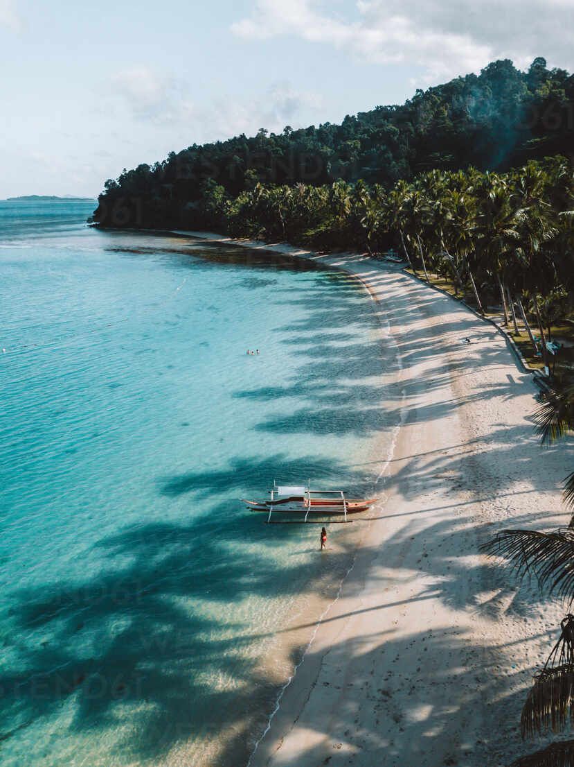 Una vista aerea di una spiaggia tropicale con una canoa a bilanciere in acqua turchese e lunghe ombre di palme sulla sabbia bianca.