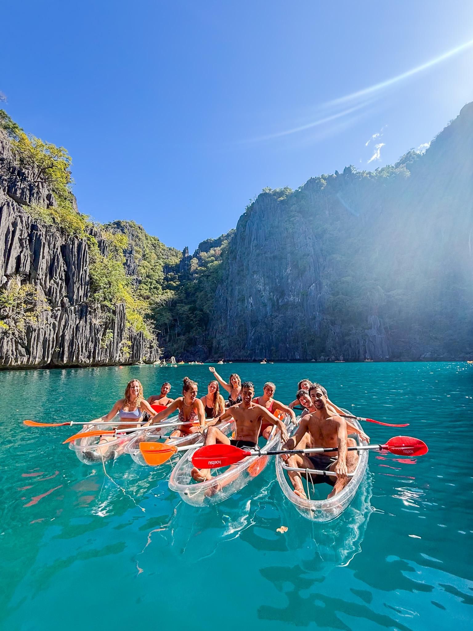 Un viaggio di gruppo WeRoad sorride per una foto in kayak trasparenti su acqua turchese accanto a scogliere rocciose.