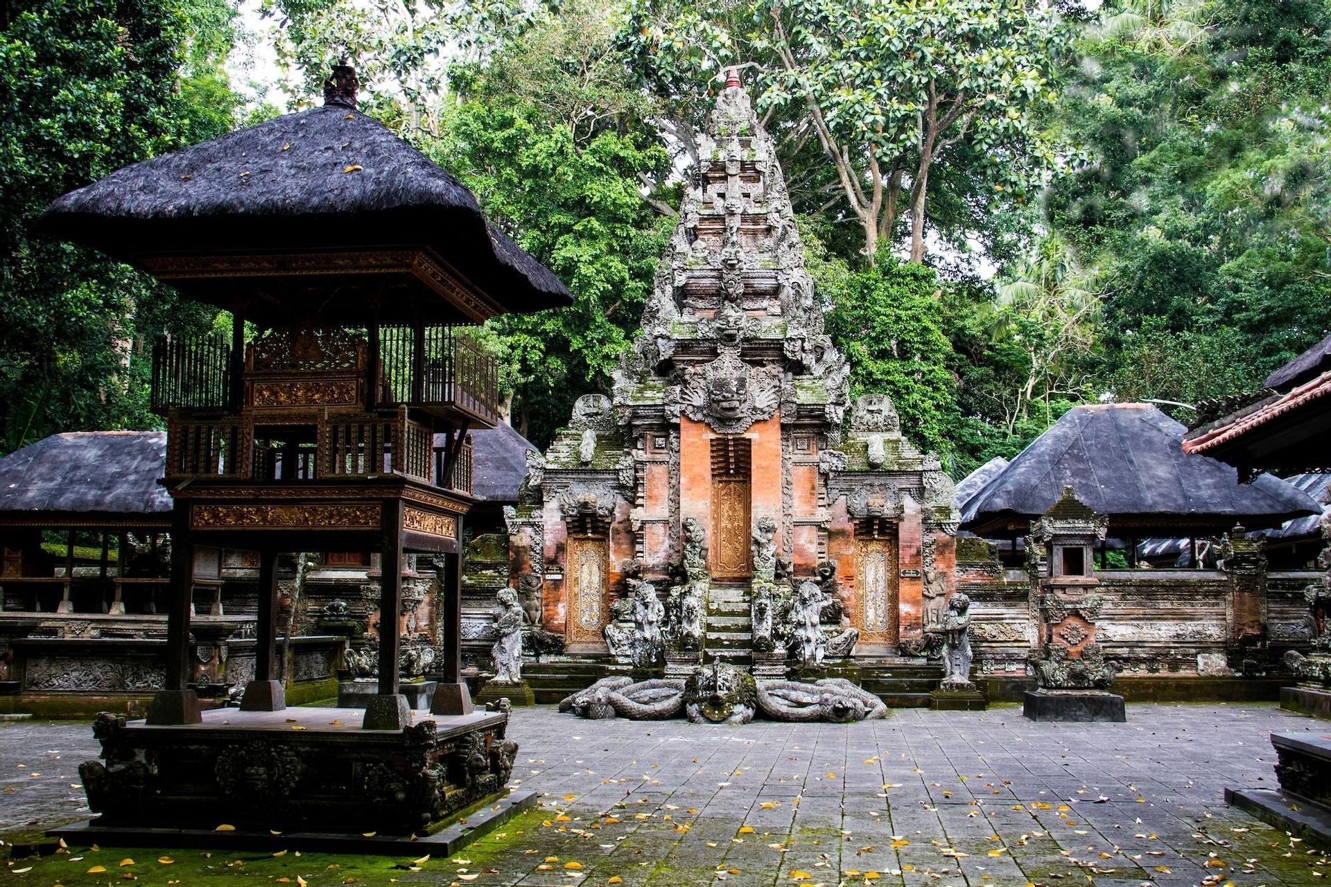Un tempio ornato con sculture in pietra e tetti di paglia si erge in un cortile circondato da una foresta lussureggiante.