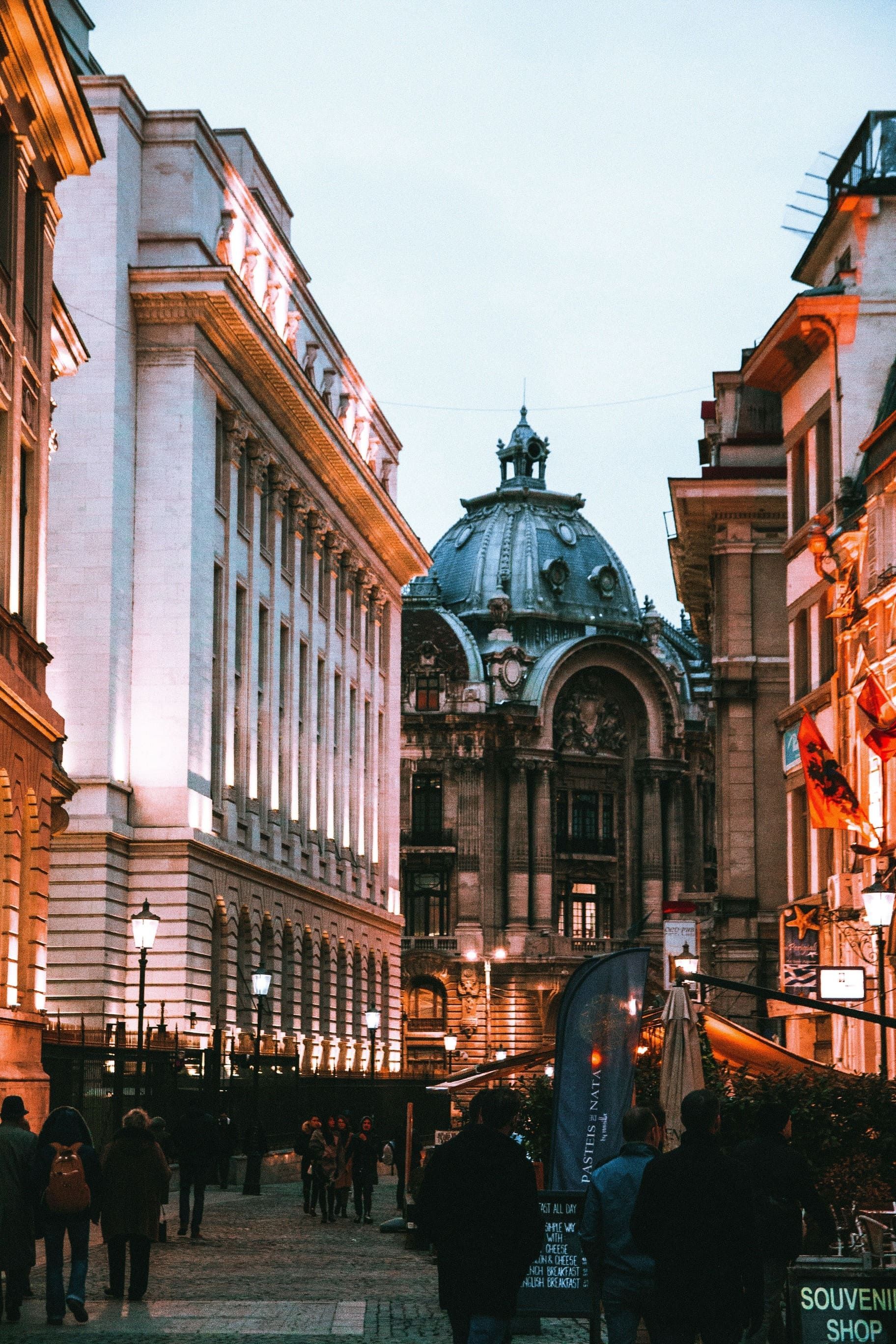 Un edificio decorato con una grande cupola si erge alla fine di una strada di ciottoli dove le persone camminano al tramonto.