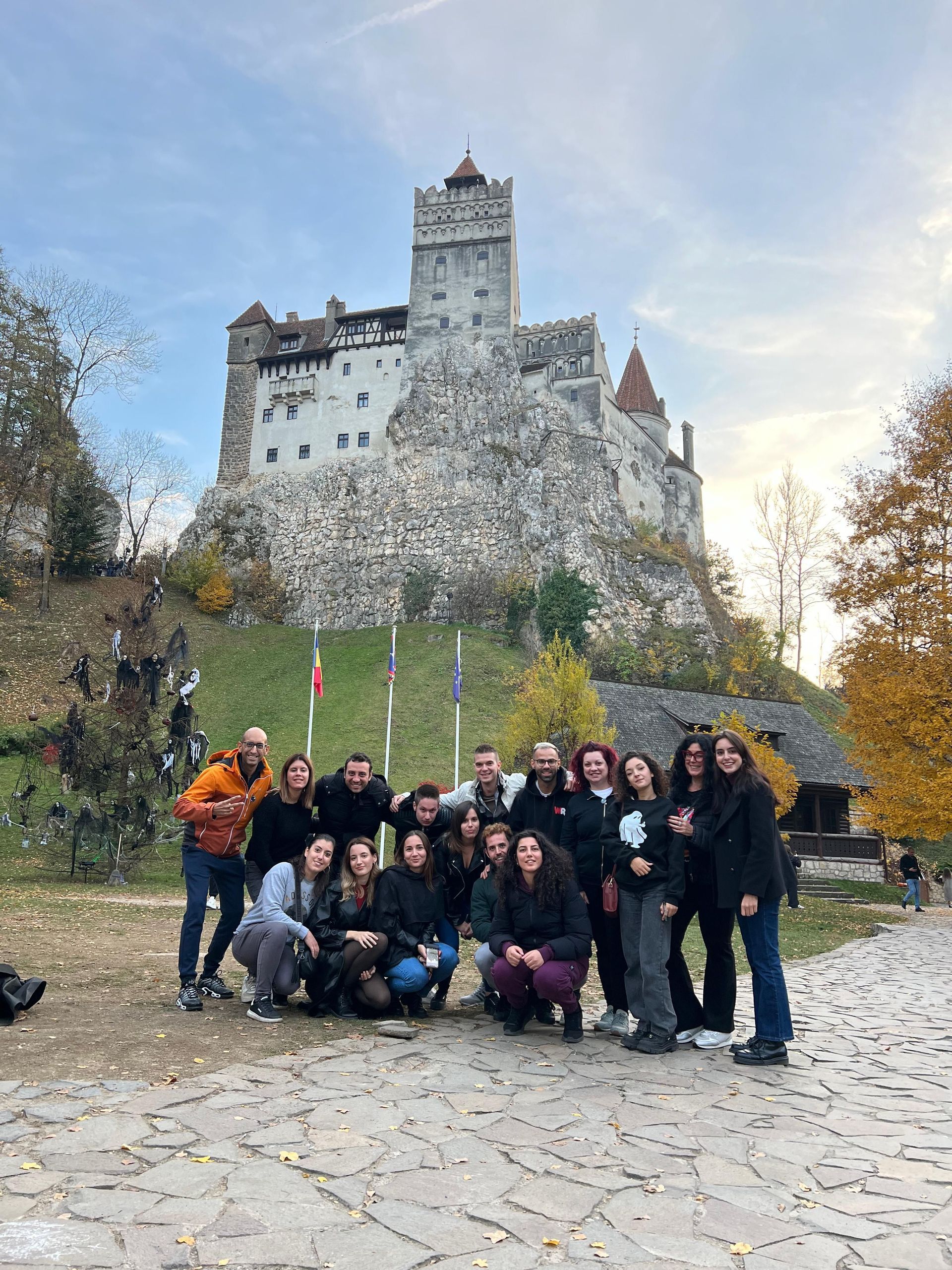 Un viaggio di gruppo WeRoad posa per una foto su un sentiero di ciottoli di fronte a un grande castello medievale su una collina rocciosa.