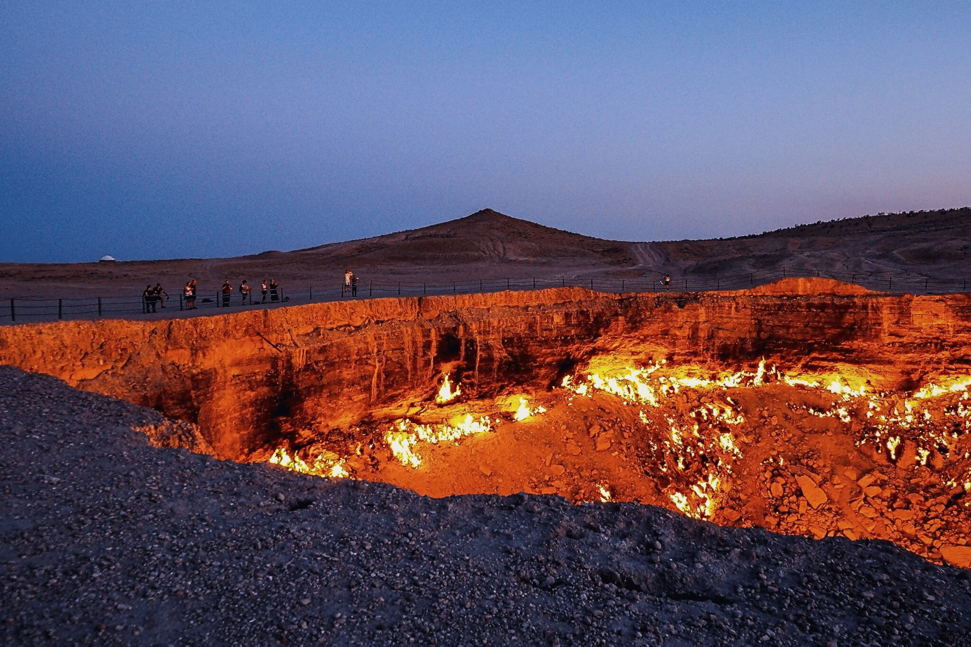 Un viaggio di gruppo WeRoad si trova sul bordo di un grande cratere infuocato al tramonto, con fiamme che illuminano le pareti rocciose.
