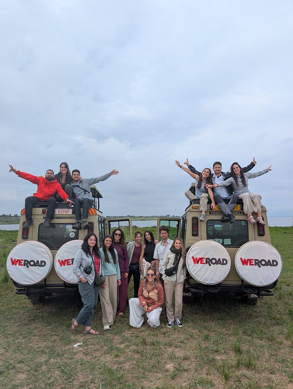 Un grupo de WeRoad posa para una foto, algunos de pie y otros sentados encima de dos vehículos de safari en un campo de hierba.