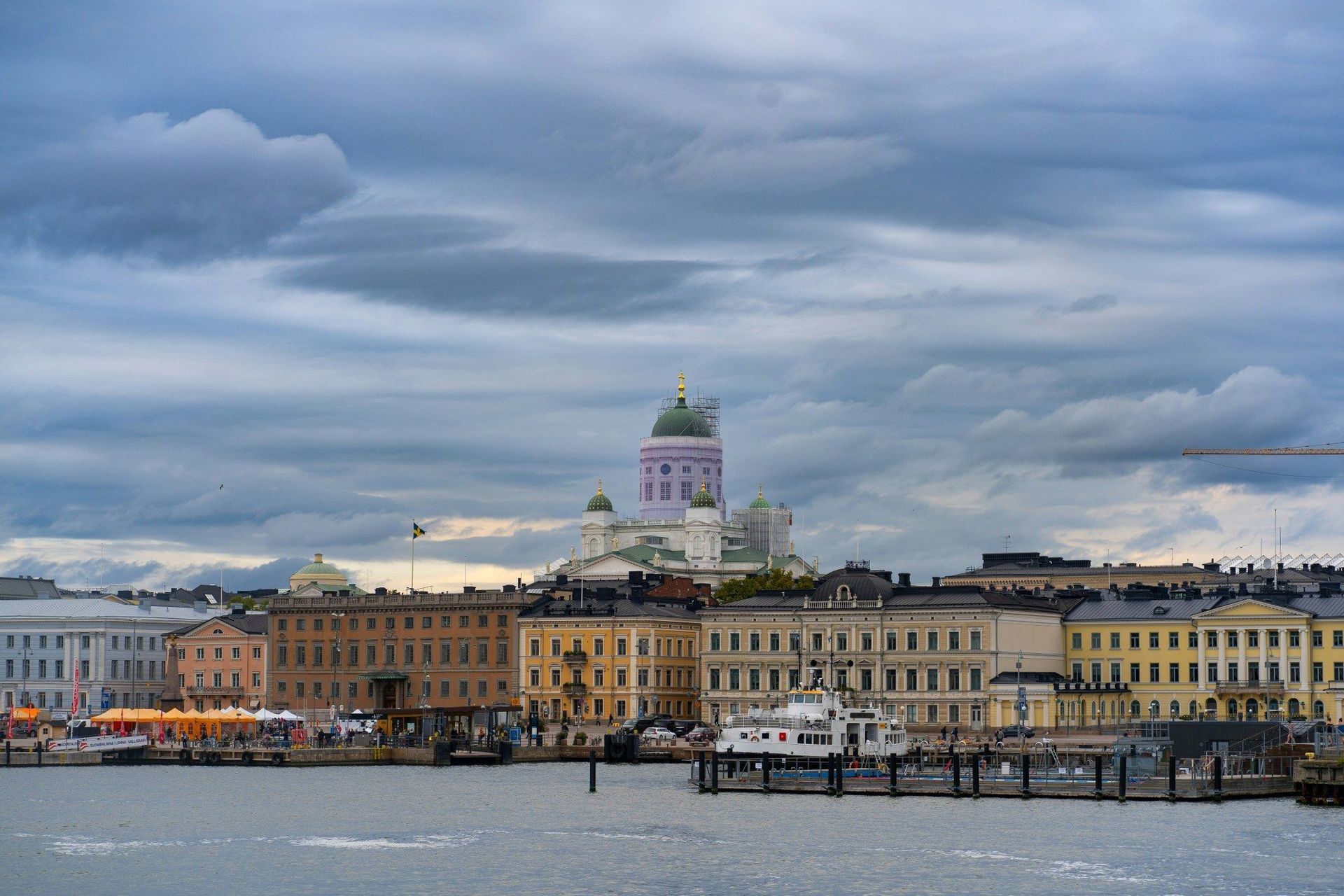 Eine Stadtsilhouette mit einem großen Dom und farbenfrohen Gebäuden, vom Wasser aus unter bewölktem Himmel gesehen.
