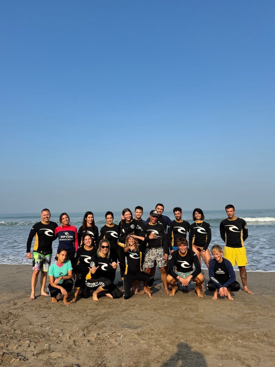 Un gruppo WeRoad in muta da sub posa per una foto su una spiaggia sabbiosa con l'oceano alle spalle.