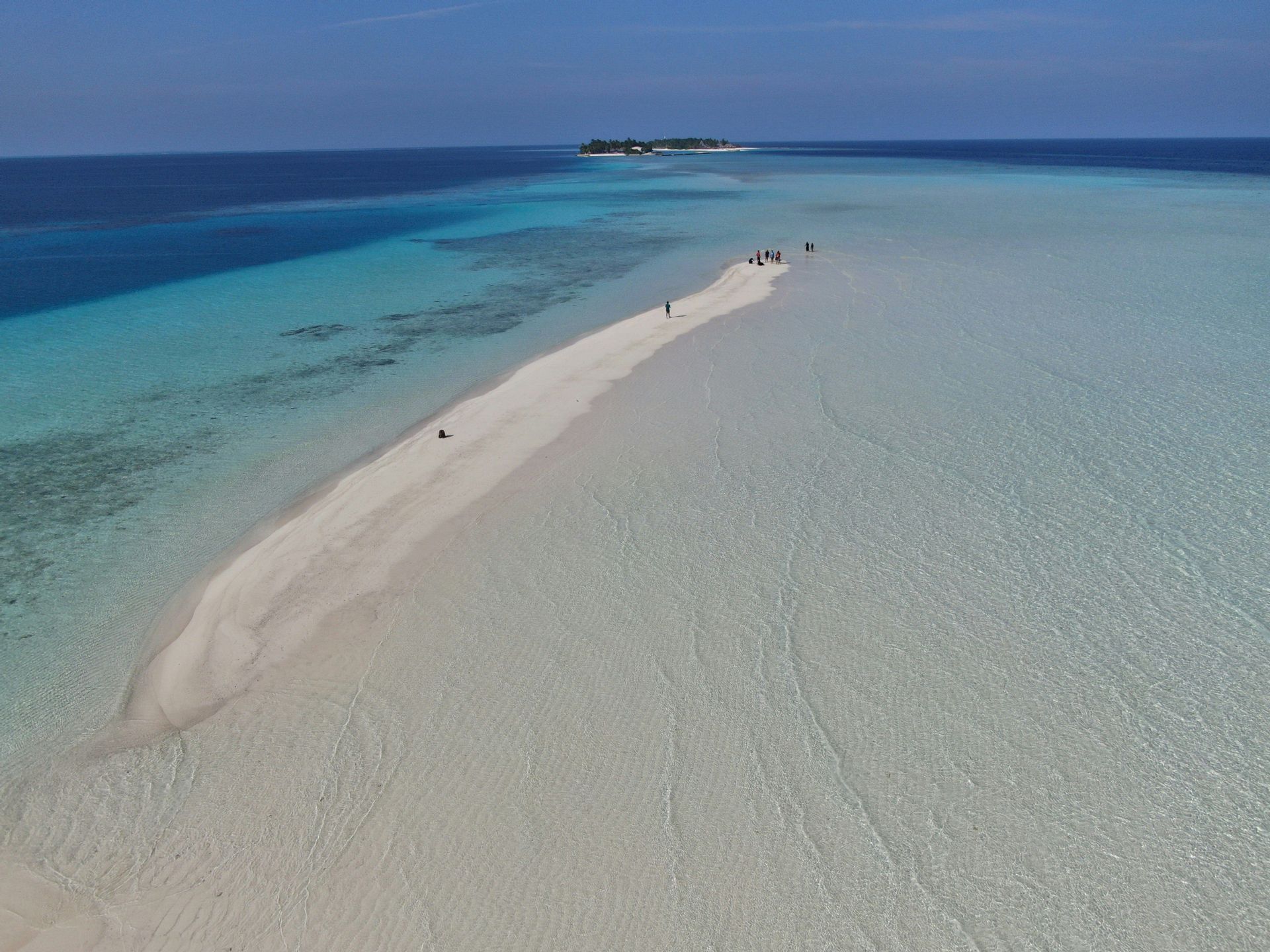 Una vista aerea di un viaggio di gruppo WeRoad che cammina lungo una lunga lingua di sabbia bianca circondata da acqua cristallina color turchese, con una piccola isola in lontananza.