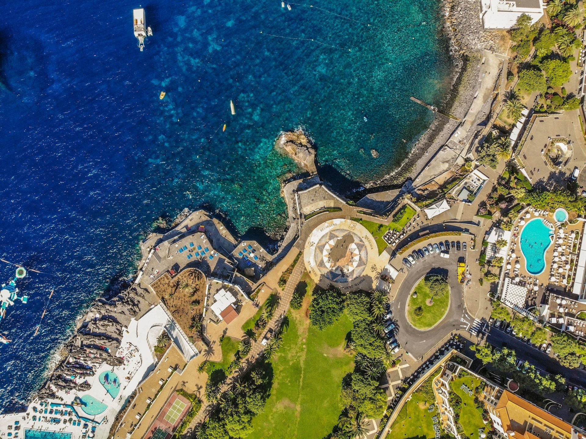 Una vista aerea, dall'alto, di un resort costiero con piscine e parchi verdi che costeggiano un oceano blu intenso.