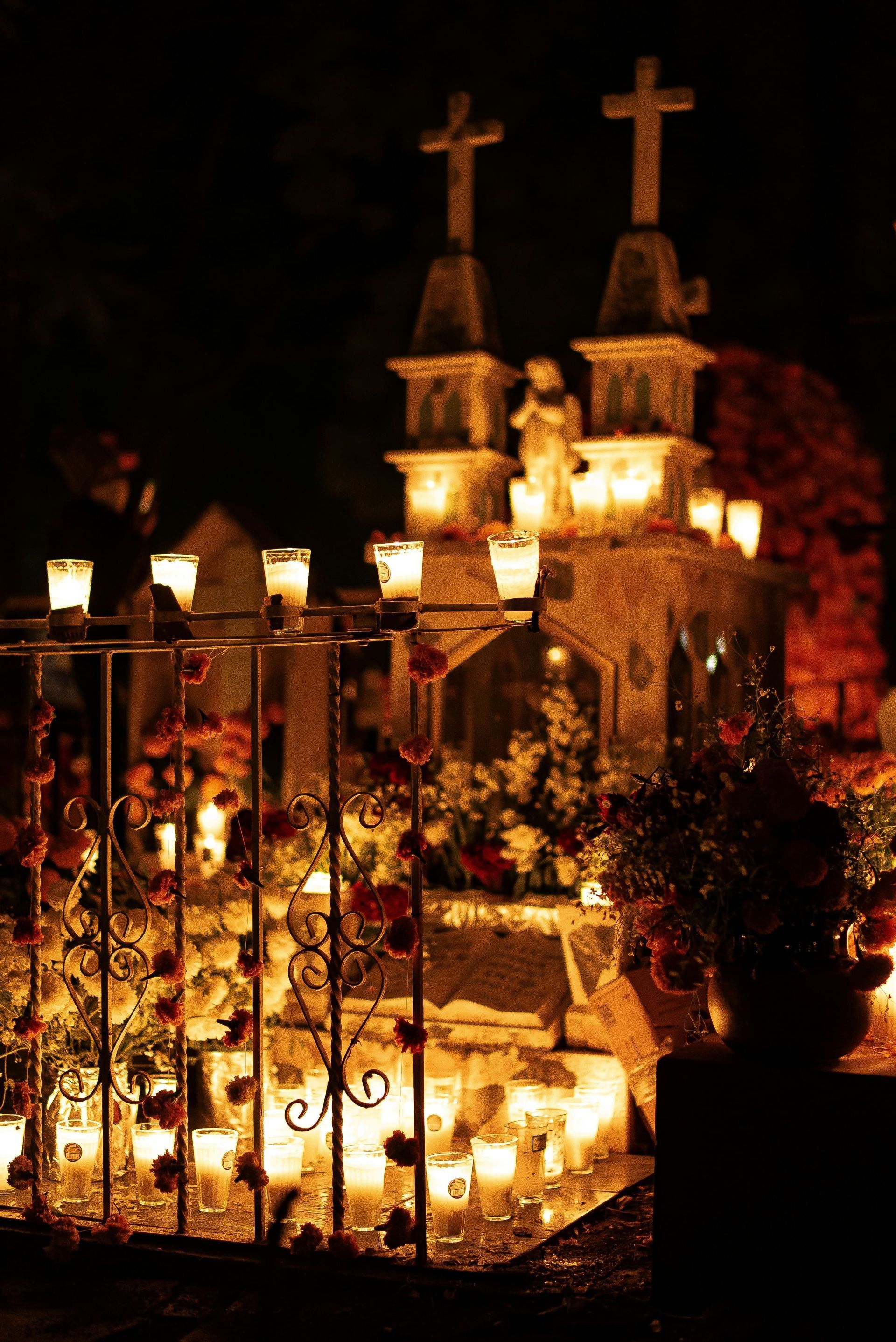 Una tomba decorata con calendule e decine di candele accese in un cimitero di notte.