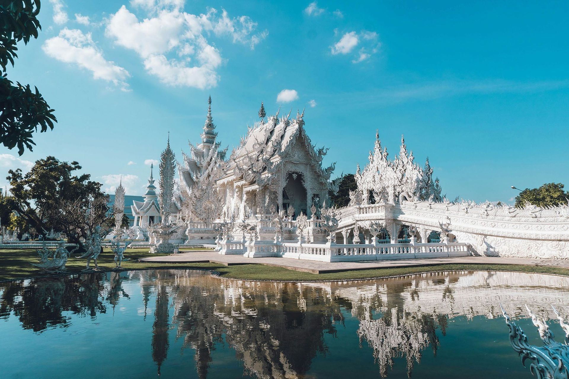 Un tempio bianco ornato con guglie intricate che si riflette in uno specchio d'acqua calmo sotto un cielo azzurro con nuvole.