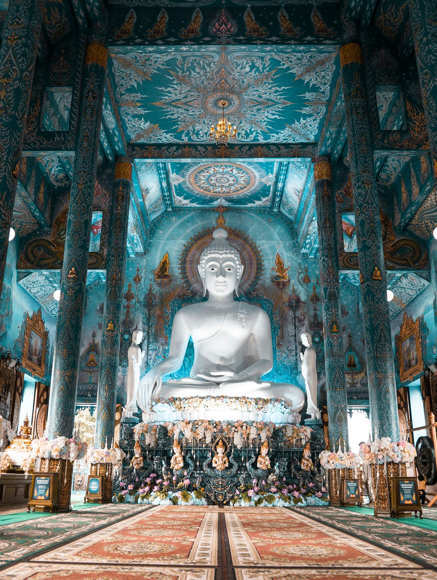 Una grande statua bianca di un Buddha seduto all'interno di un tempio con intricate decorazioni blu e oro su pareti e soffitto.