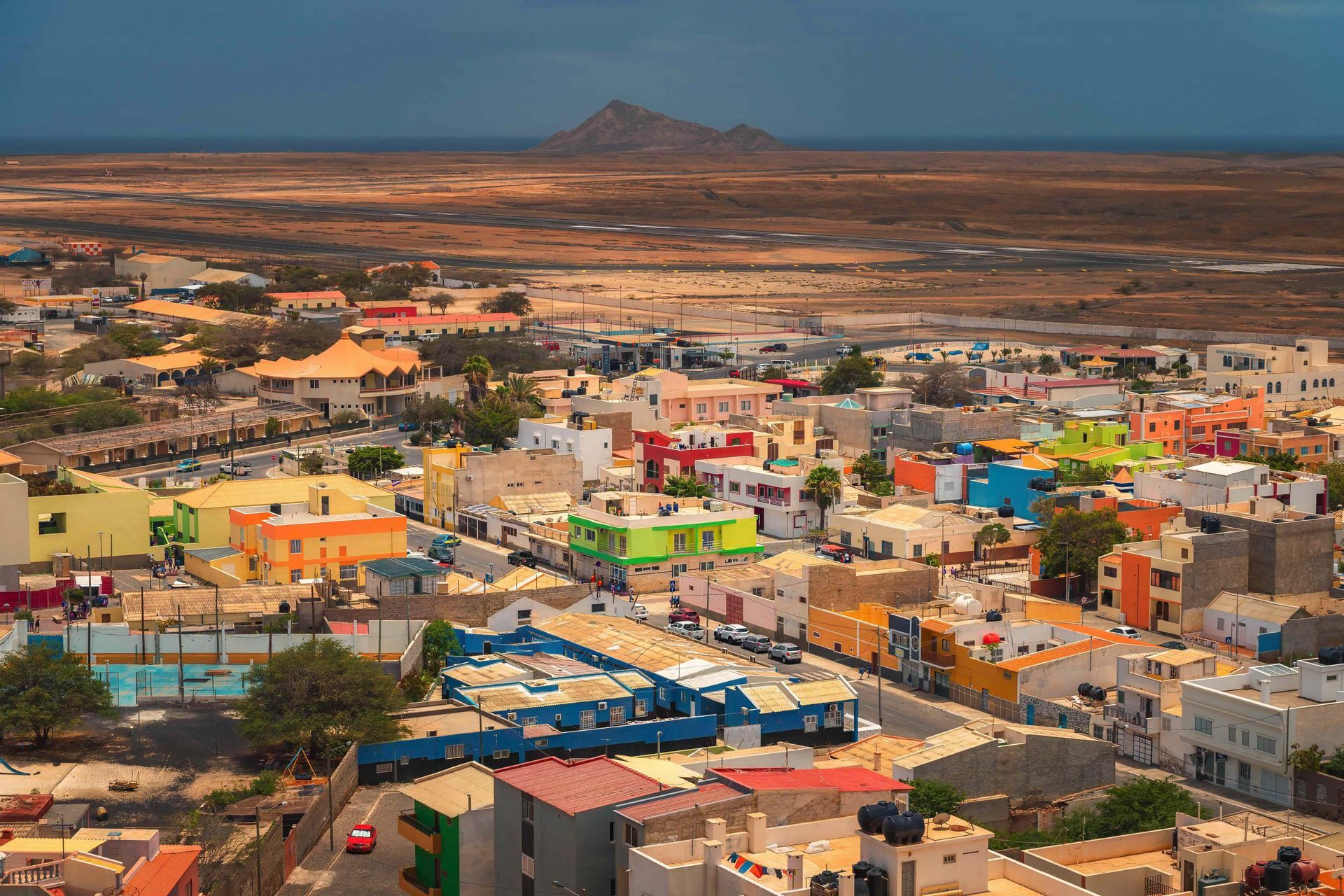 Vue en hauteur d'une ville colorée avec des bâtiments bas dans un vaste paysage aride avec une montagne à l'horizon.