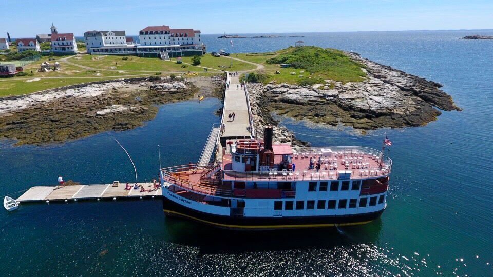 Una vista aerea di una grande barca da turismo attraccata a un lungo molo collegato a un'isola erbosa con diversi edifici bianchi.