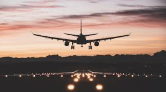 An airplane seen from behind as it prepares to land on an illuminated runway at sunset.