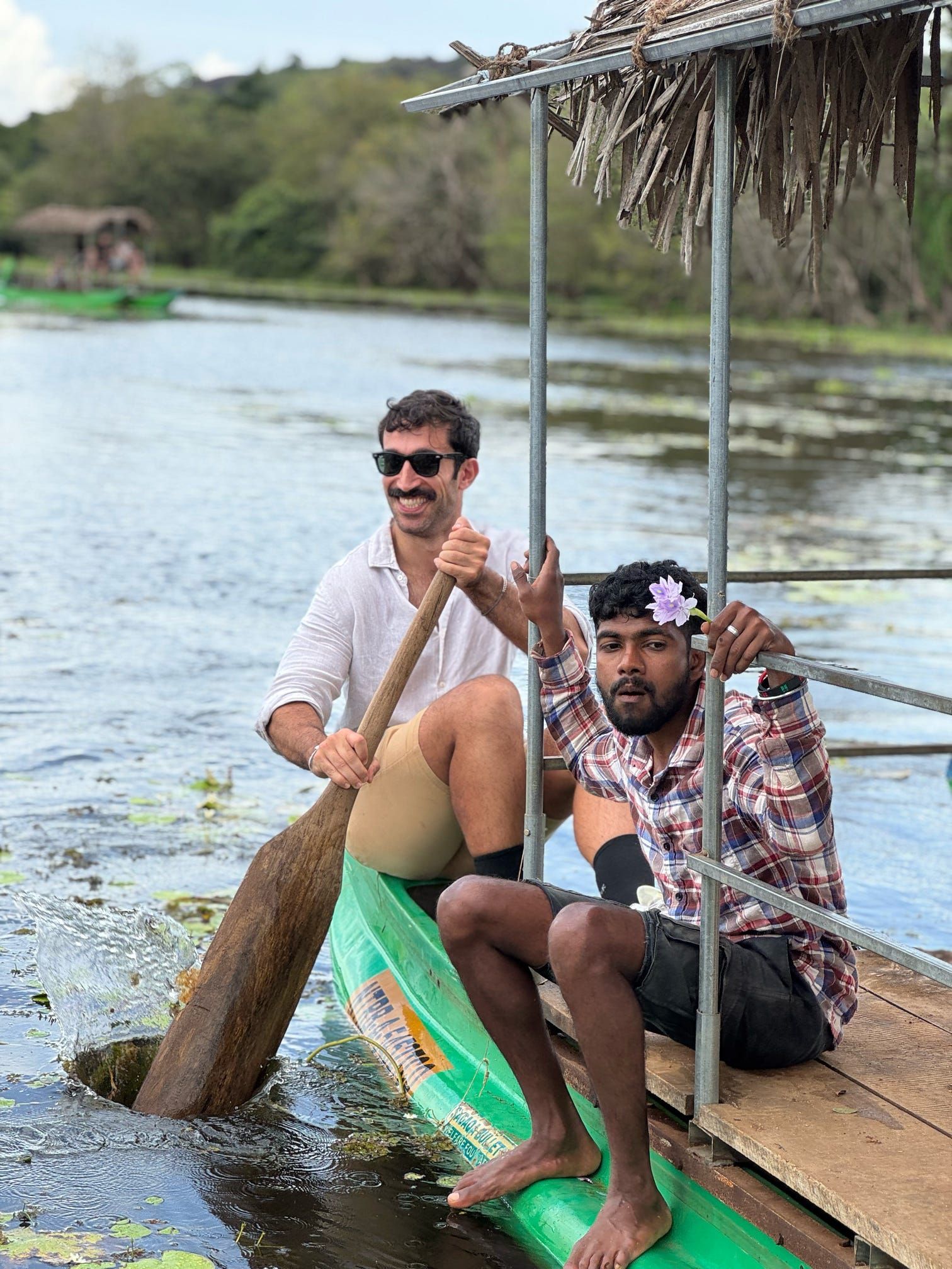 Zwei Männer einer WeRoad Gruppenreise in einem grünen Kanu auf einem See, einer paddelnd und der andere auf der Plattform sitzend.